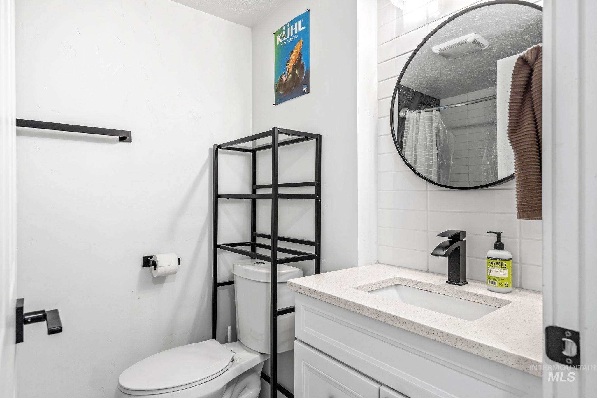 Bathroom featuring a white vanity with an integrated sink, a dark bronze waterfall faucet, and a round wall-mounted mirror