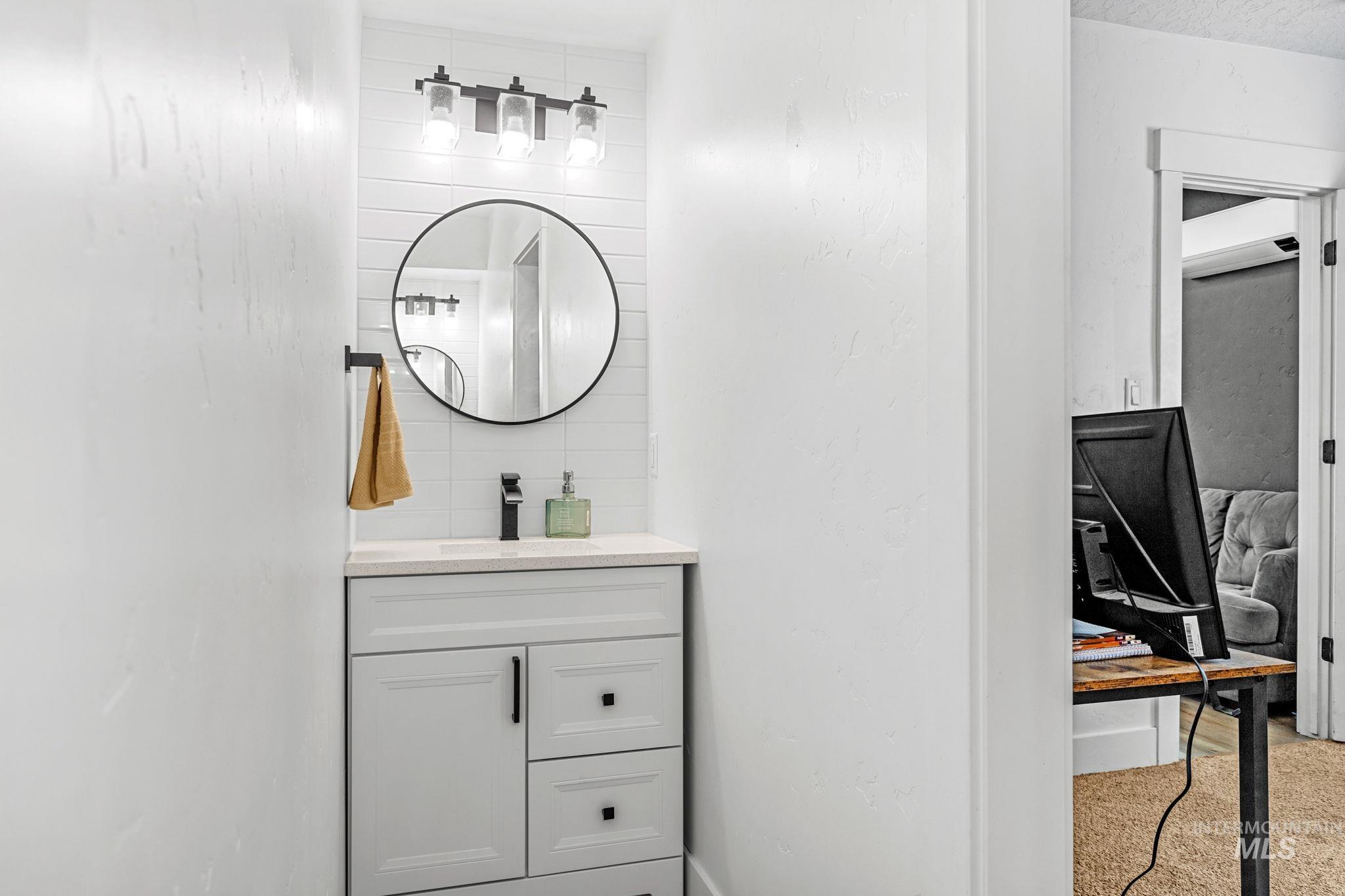 Compact vanity featuring a white cabinet with black hardware, a light-toned countertop, and a circular wall mirror