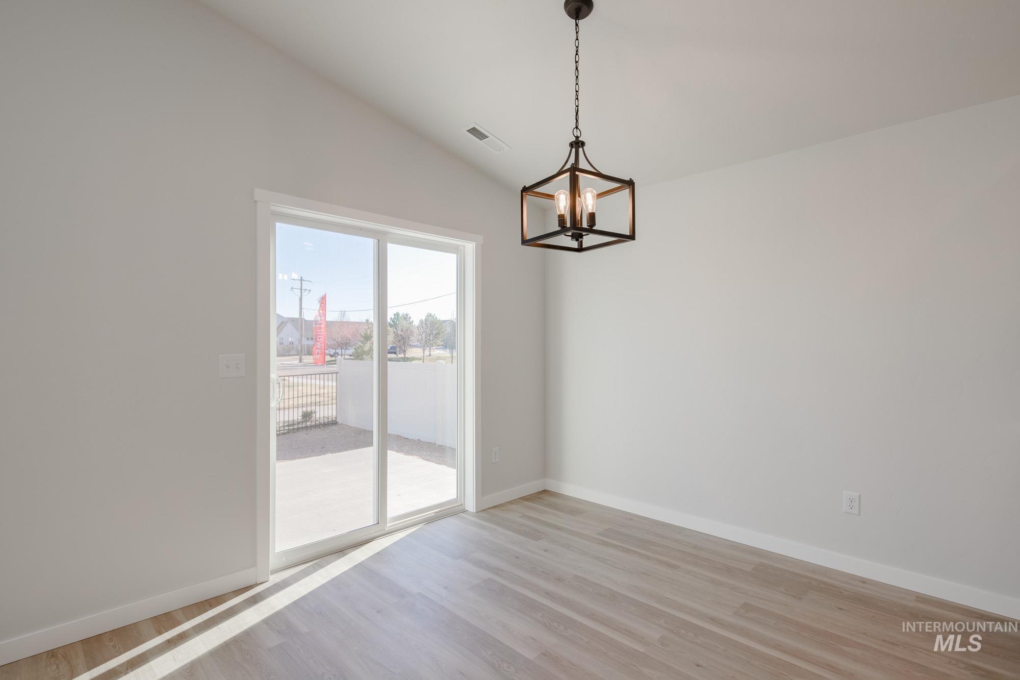 Unfurnished dining area featuring light wood-style flooring, lofted ceiling, and a chandelier