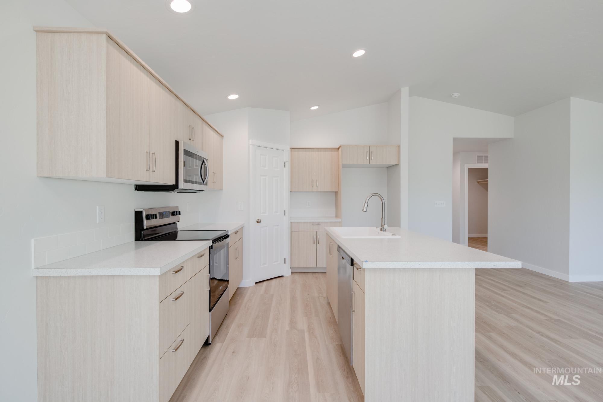 Kitchen with appliances with stainless steel finishes, light brown cabinetry, light wood-style floors, a center island with sink, and modern cabinets