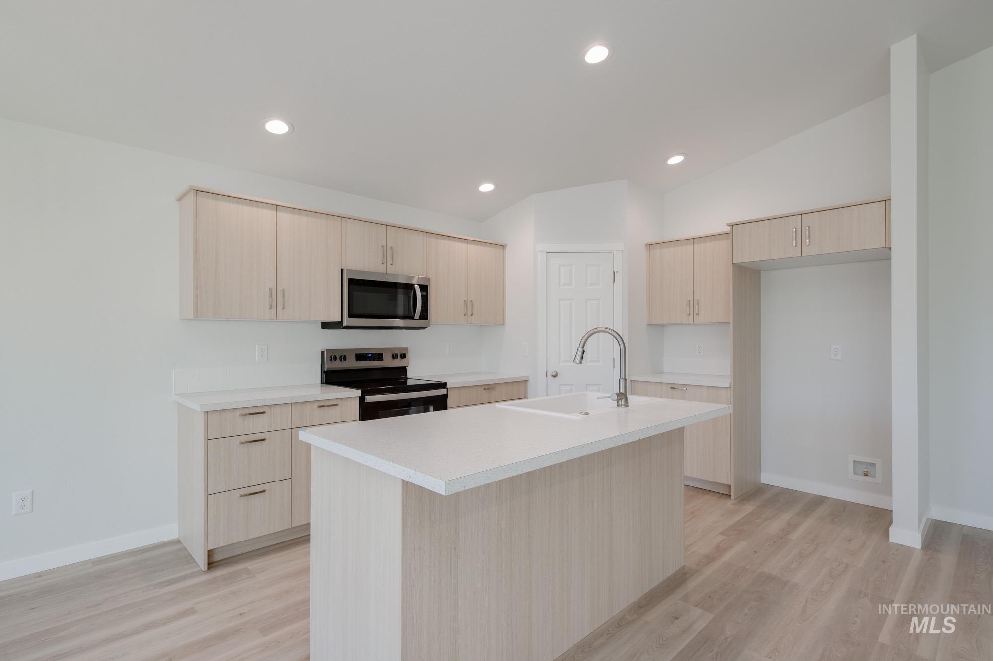 Kitchen featuring light brown cabinetry, stainless steel appliances, light countertops, modern cabinets, and light wood-type flooring