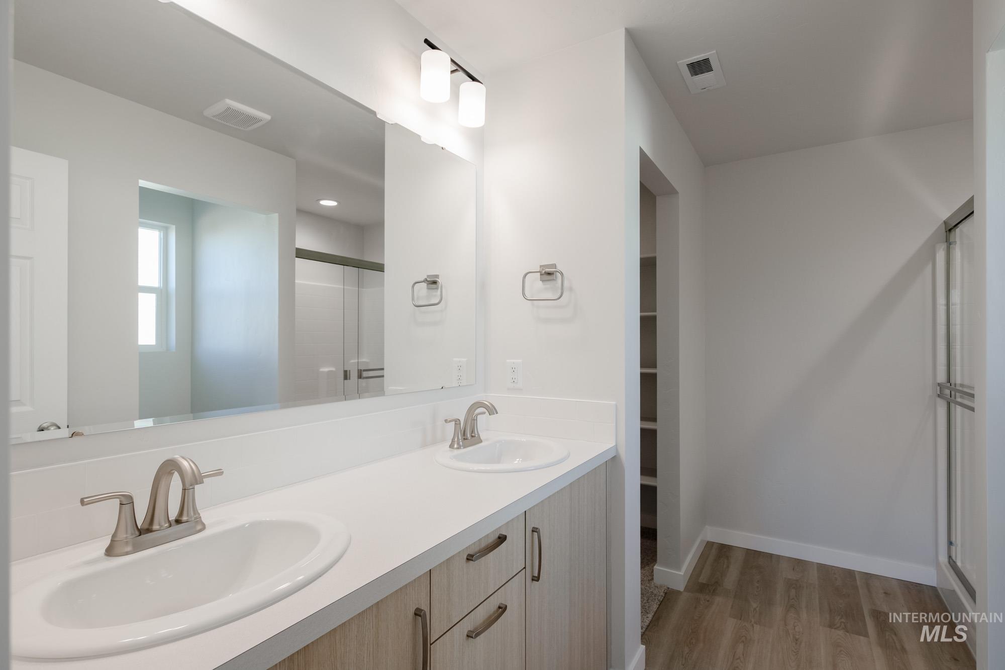 Bathroom featuring a stall shower, double vanity, light wood-type flooring, and a spacious closet