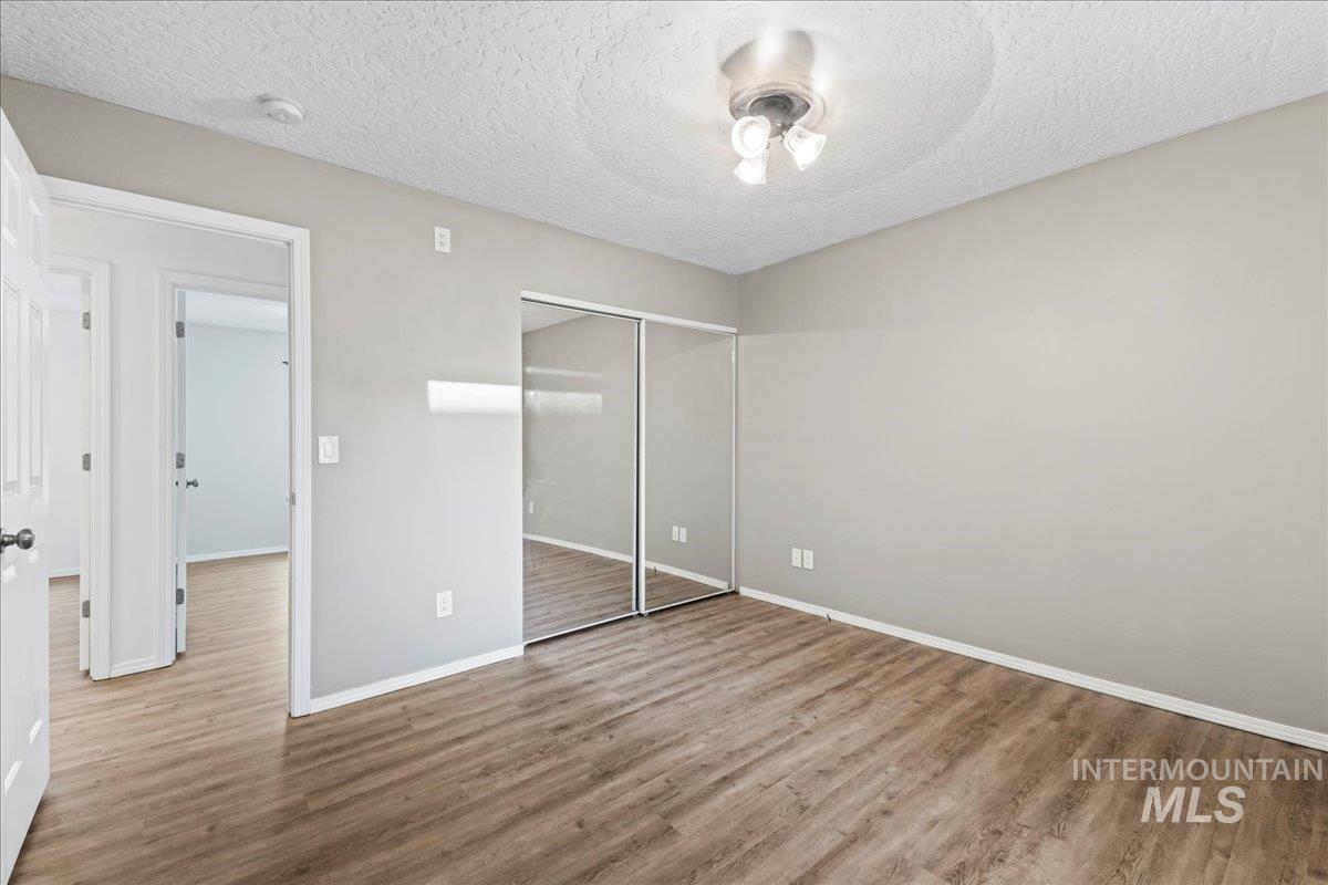 Unfurnished bedroom featuring a textured ceiling, wood finished floors, a closet, and a ceiling fan
