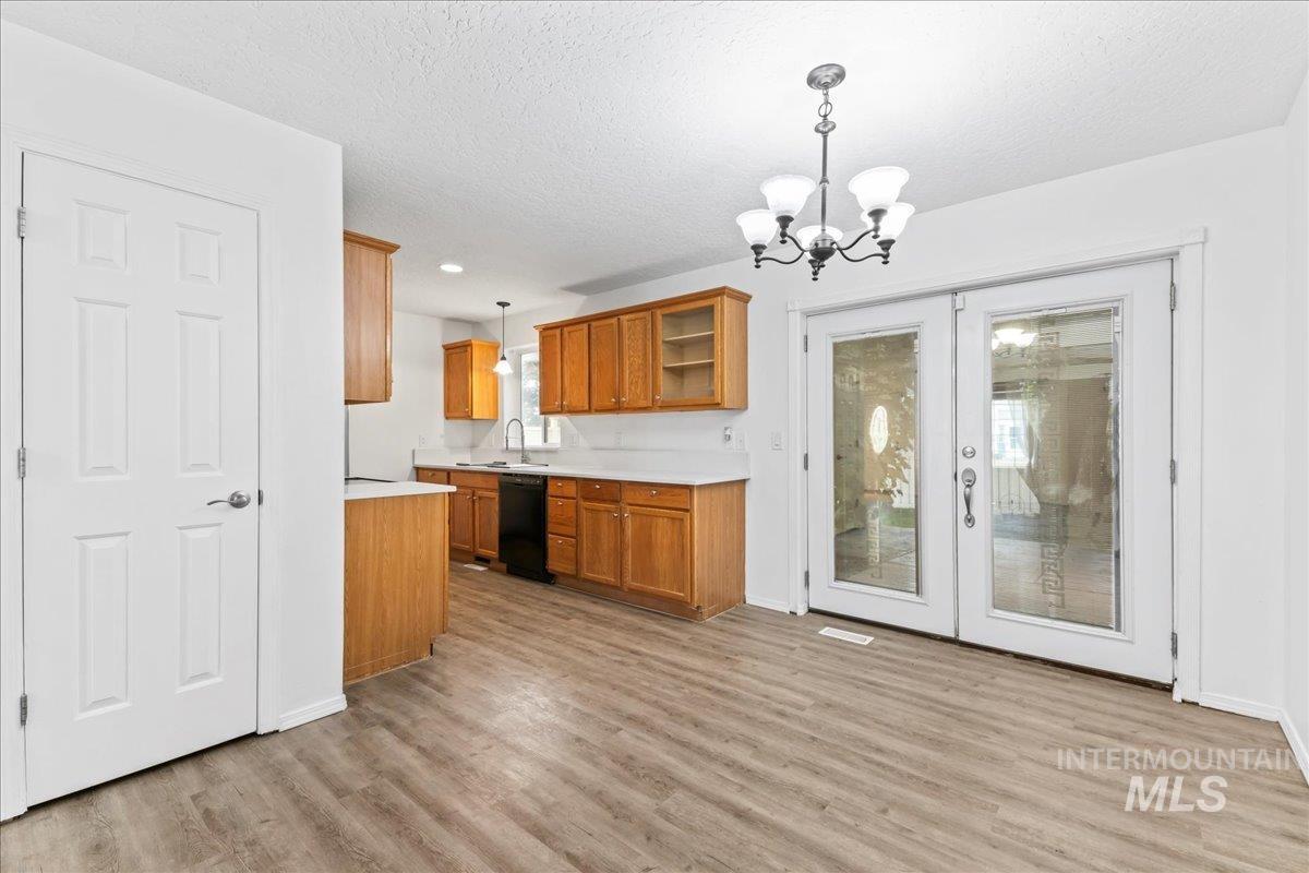 Kitchen featuring decorative light fixtures, light countertops, brown cabinetry, french doors, and light wood finished floors