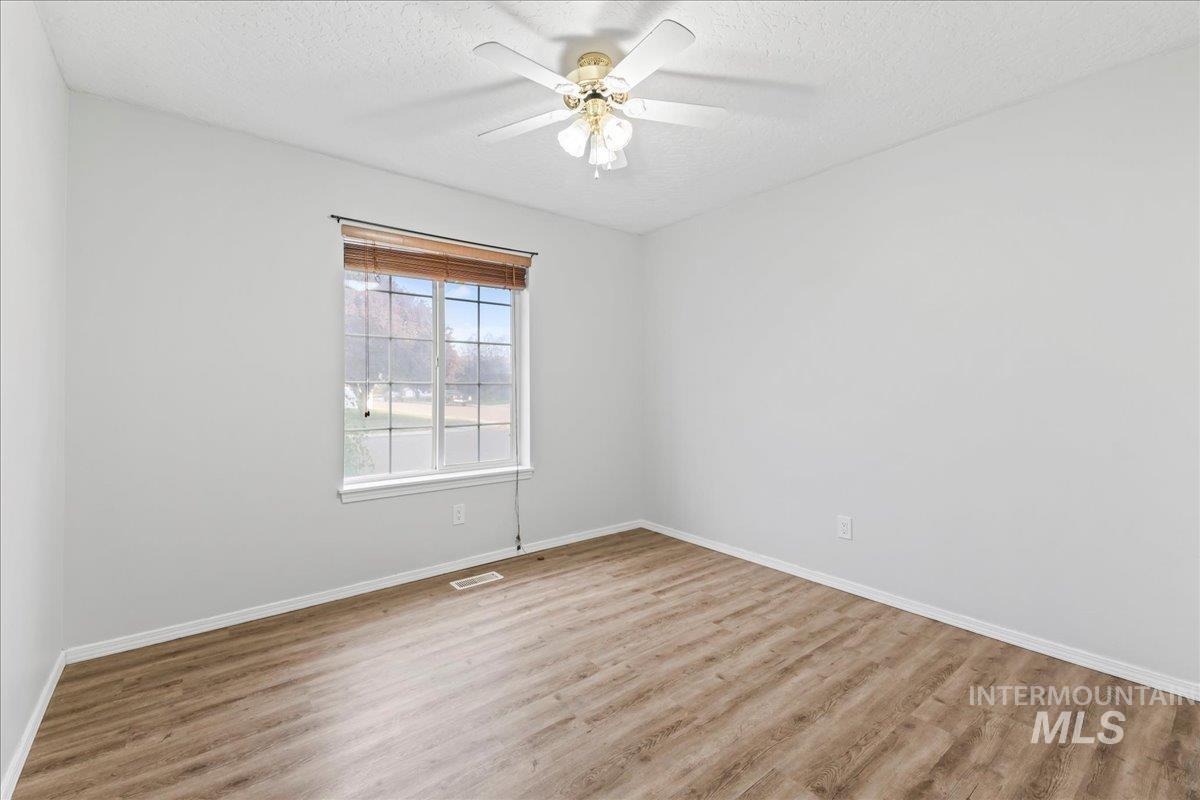 Unfurnished room featuring light wood-style floors, a textured ceiling, and a ceiling fan