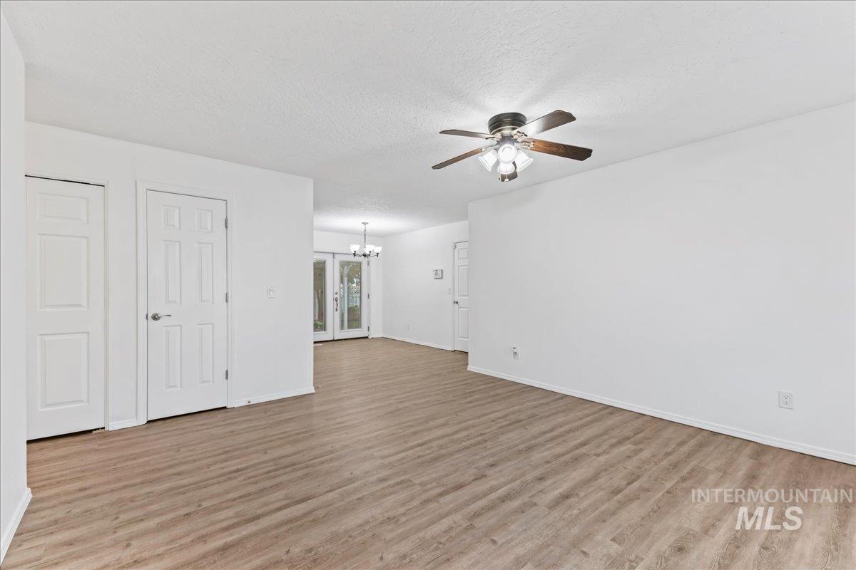 Unfurnished living room featuring a textured ceiling, light wood-type flooring, a ceiling fan, and a chandelier