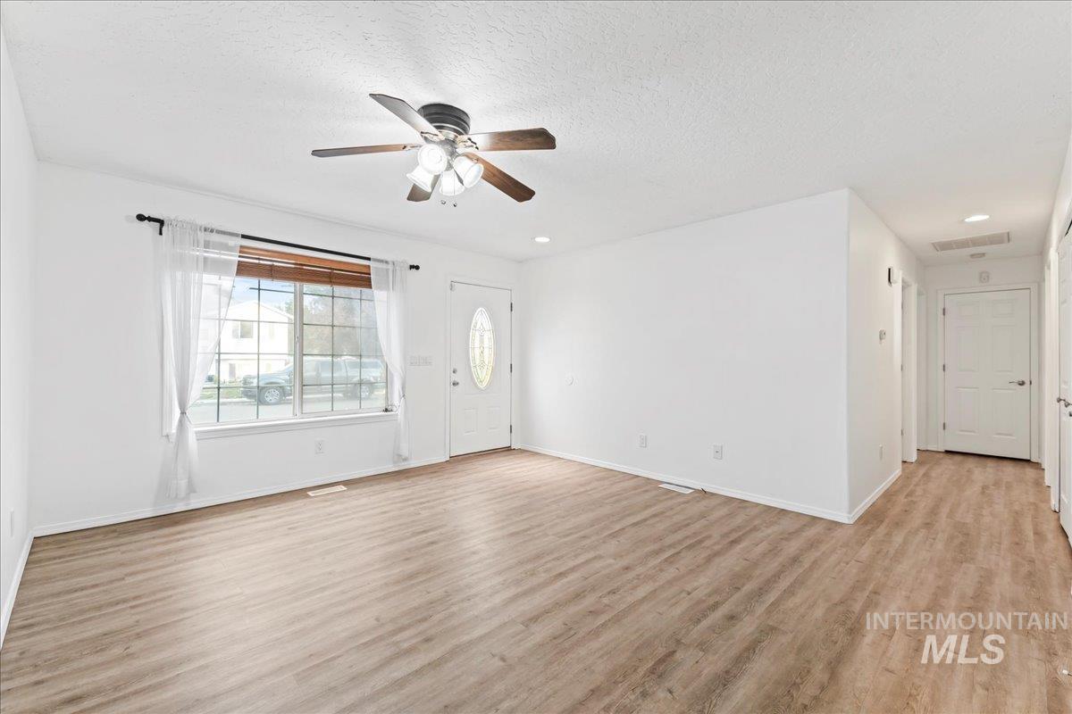 Unfurnished living room featuring light wood-style flooring, ceiling fan, and a textured ceiling