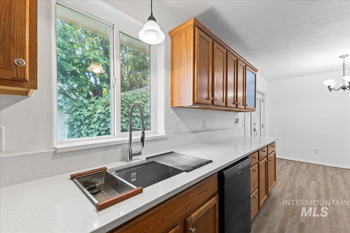 Kitchen featuring pendant lighting, brown cabinetry, black dishwasher, light stone countertops, and a textured ceiling