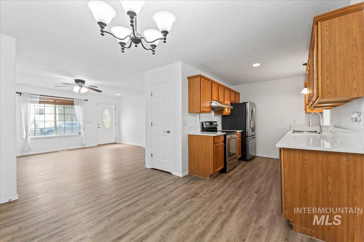 Kitchen with hanging light fixtures, stainless steel range with electric stovetop, brown cabinets, dark wood-style floors, and a chandelier