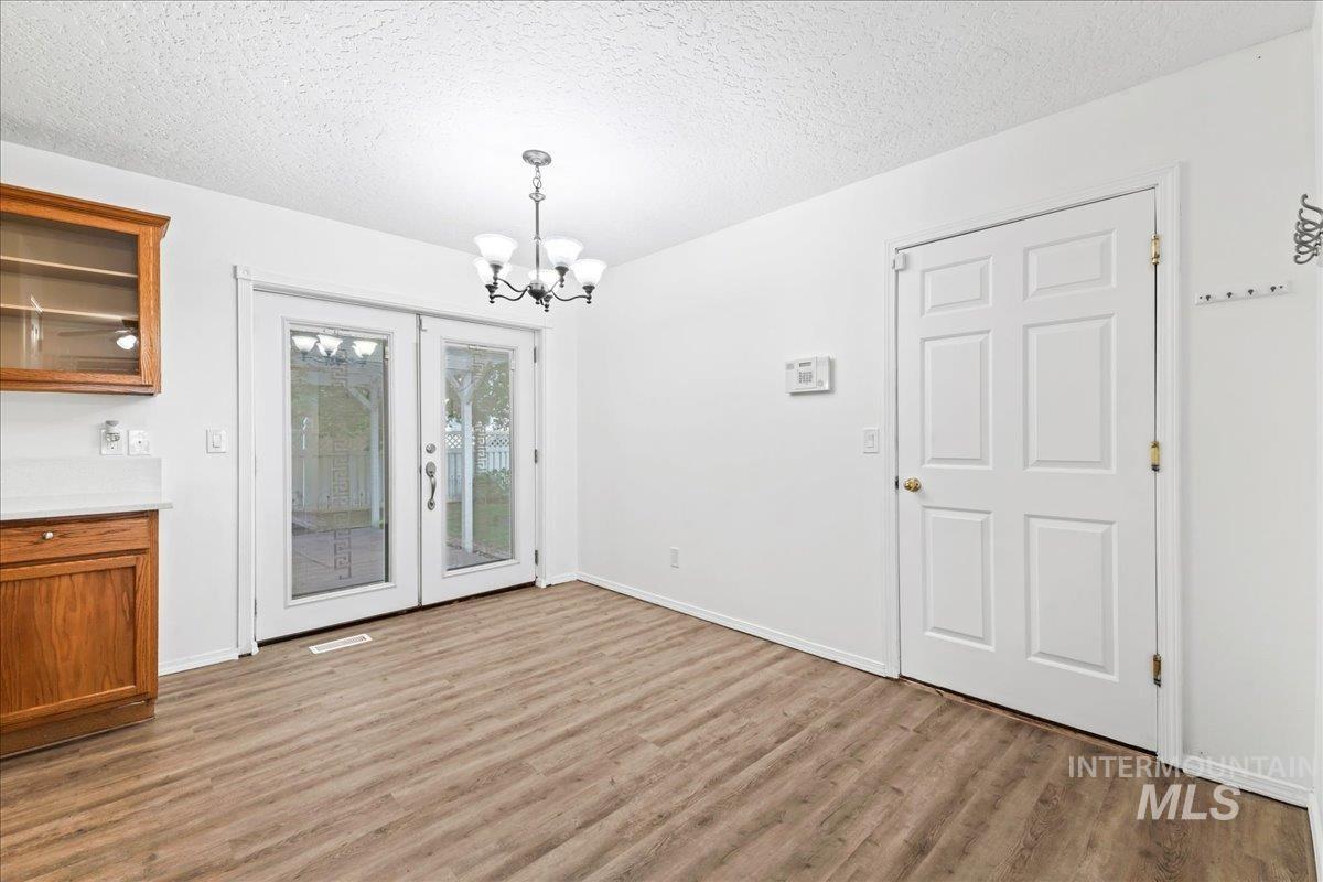 Unfurnished dining area featuring a textured ceiling, light wood finished floors, a chandelier, and french doors