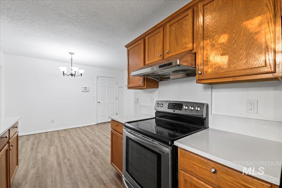 Kitchen with electric stove, brown cabinets, under cabinet range hood, light wood-type flooring, and a textured ceiling