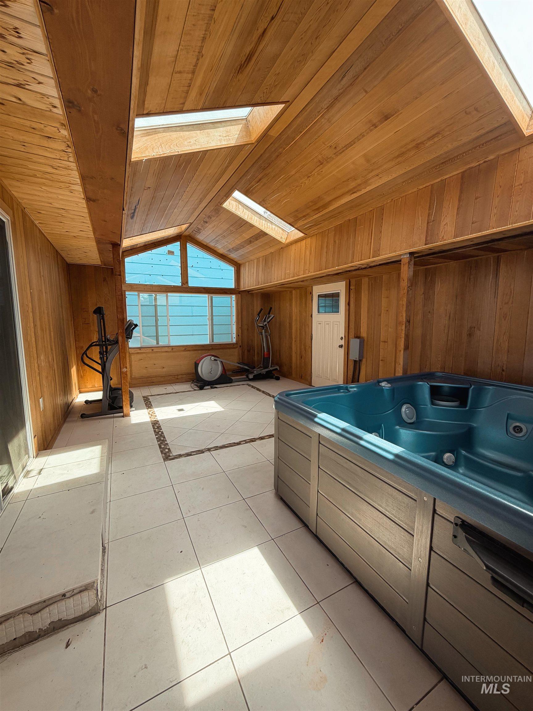 Enclosed sunroom featuring a built-in hot tub, wood-paneled walls and ceiling, multiple skylights, and large windows