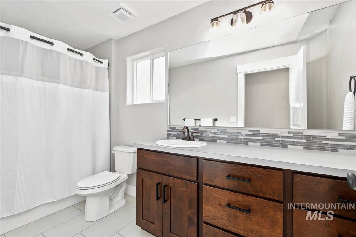 Bathroom with a shower with curtain, vanity, decorative backsplash, and light tile patterned floors