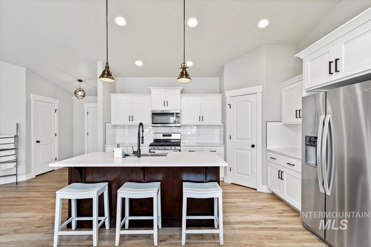 Kitchen with appliances with stainless steel finishes, white cabinets, an island with sink, hanging light fixtures, and a kitchen breakfast bar