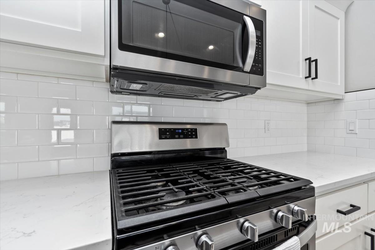 Kitchen view of appliances with stainless steel finishes, light stone countertops, white cabinetry, and tasteful backsplash
