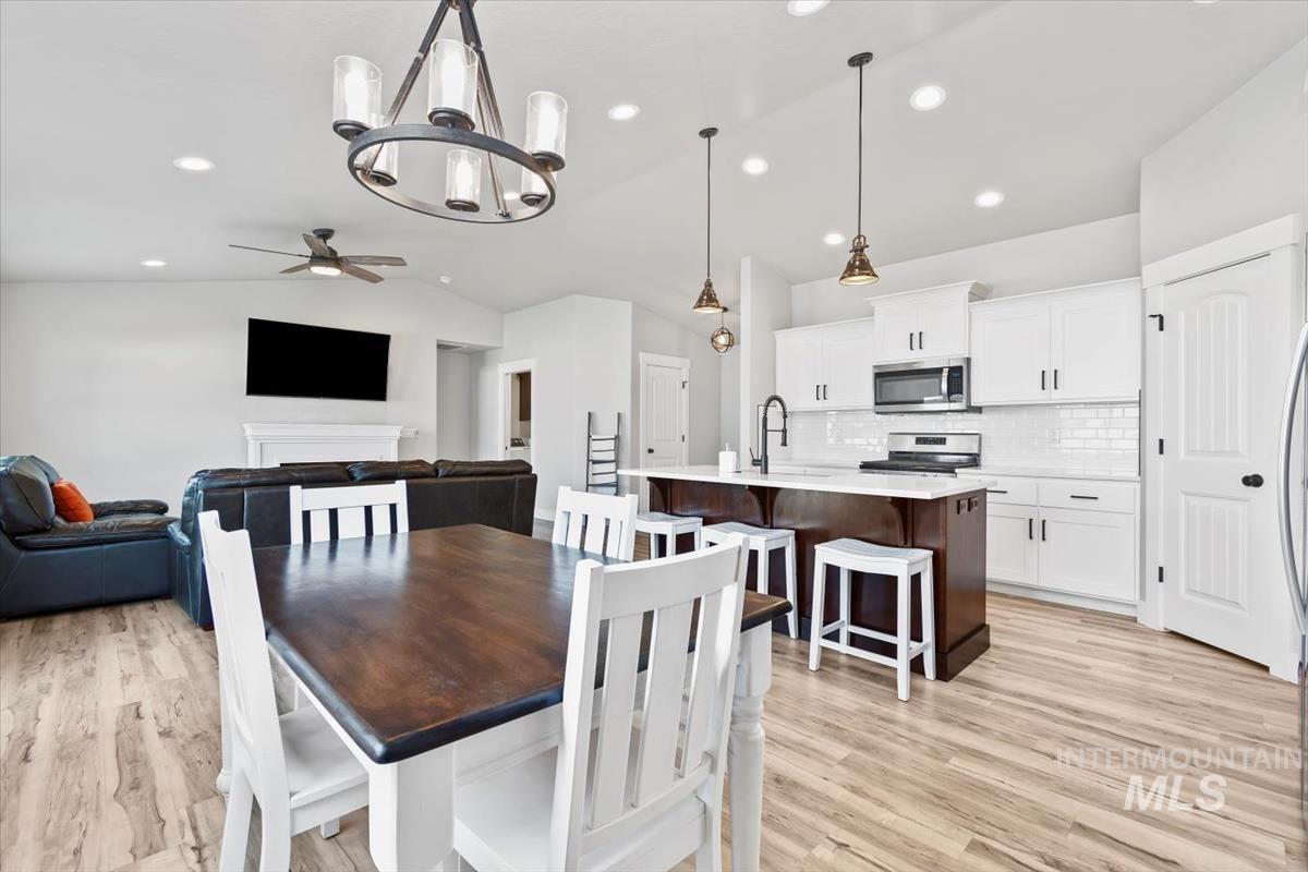 Dining area featuring a chandelier, vaulted ceiling, ceiling fan, light wood-style floors, and recessed lighting