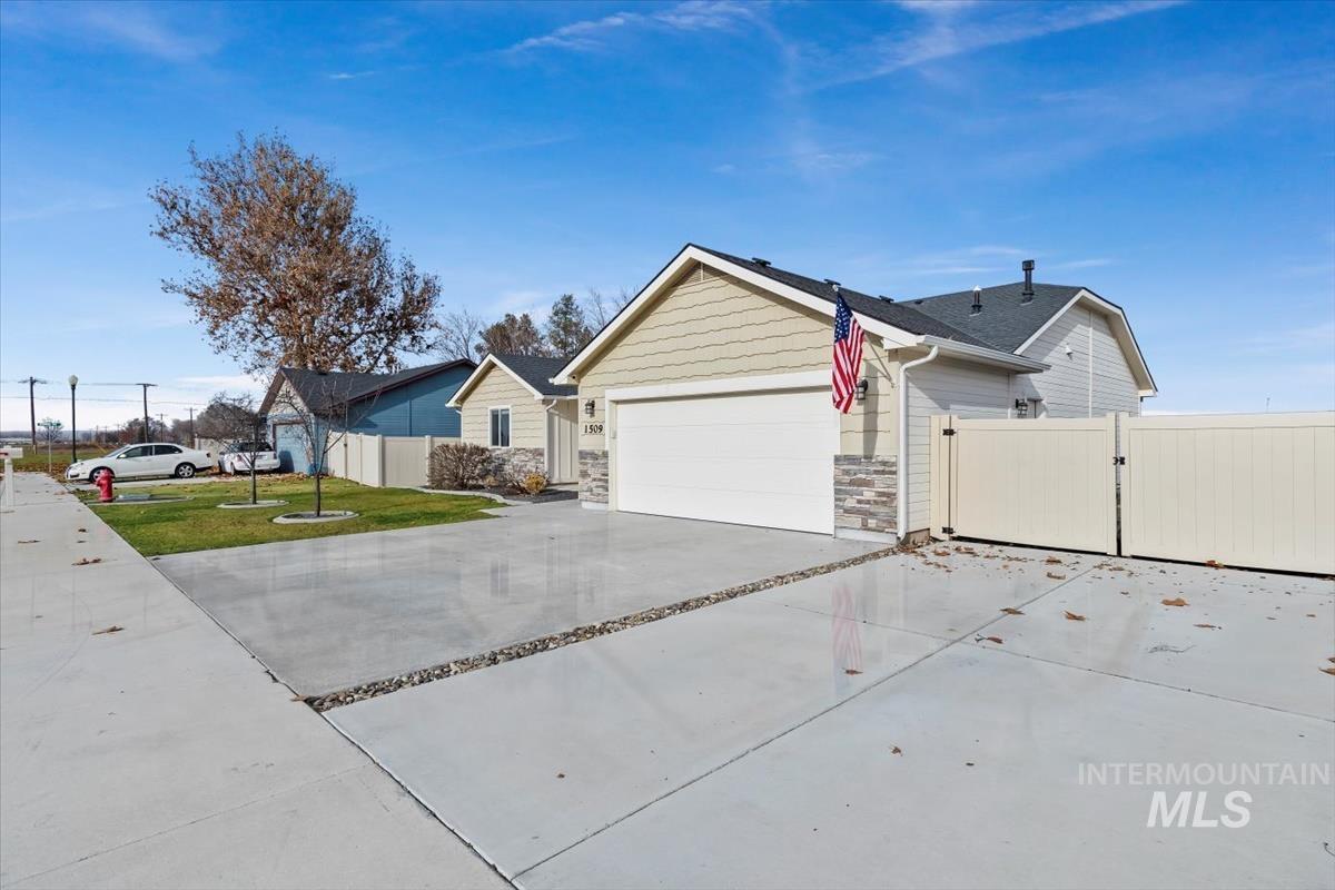 View of side of home with concrete driveway, a gate, stone siding, and an attached garage