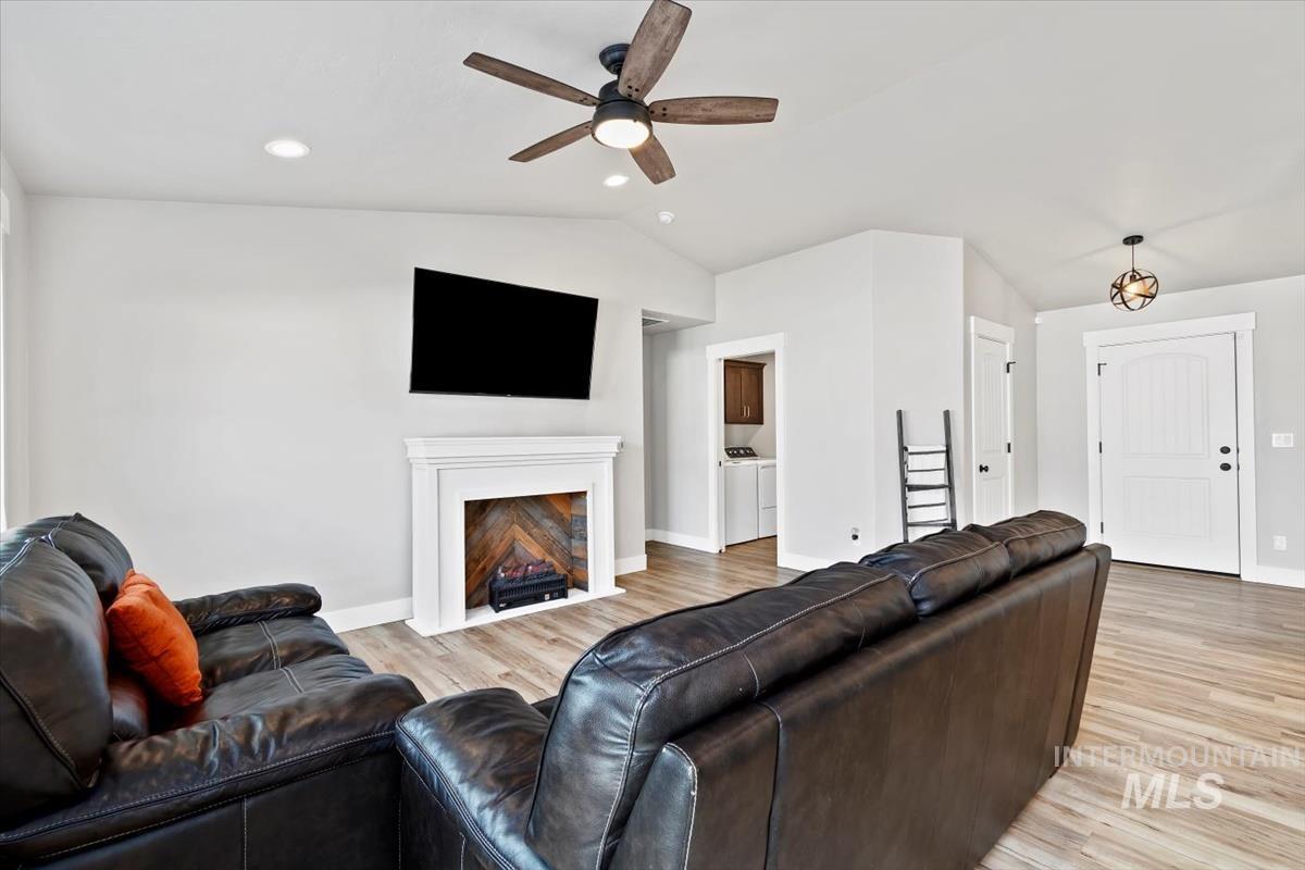 Living area with vaulted ceiling, light wood-style floors, ceiling fan, a fireplace, and separate washer and dryer