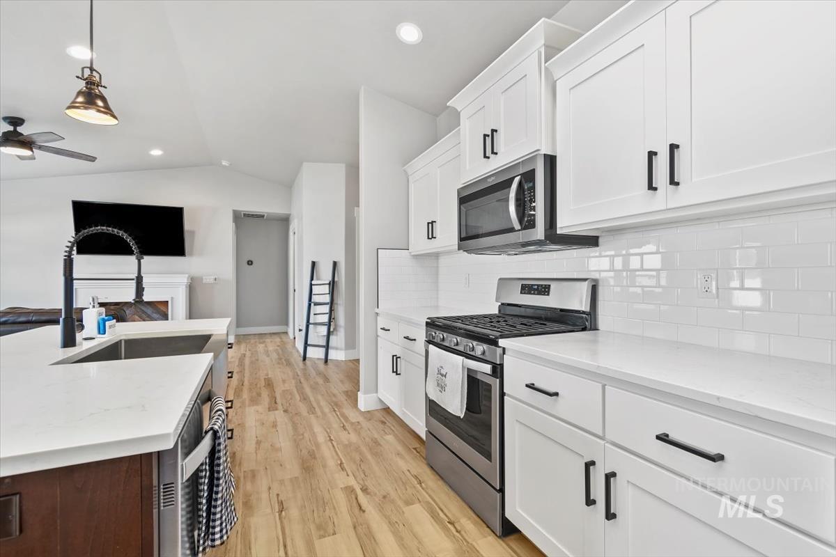 Kitchen with stainless steel appliances, pendant lighting, lofted ceiling, white cabinets, and light stone countertops