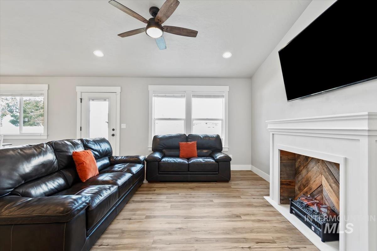 Living room with light wood-style flooring, plenty of natural light, a lit fireplace, recessed lighting, and a ceiling fan