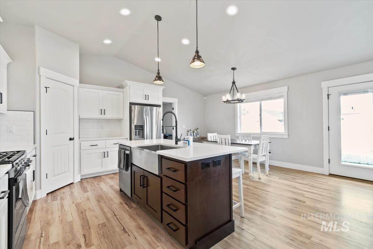 Kitchen with hanging light fixtures, an island with sink, dark brown cabinetry, white cabinetry, and backsplash