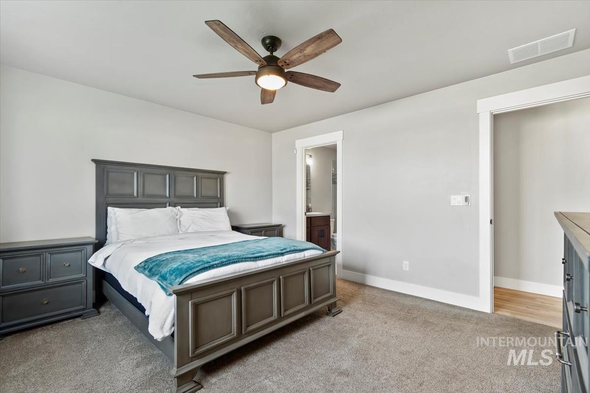 Bedroom with light colored carpet, a ceiling fan, and ensuite bath