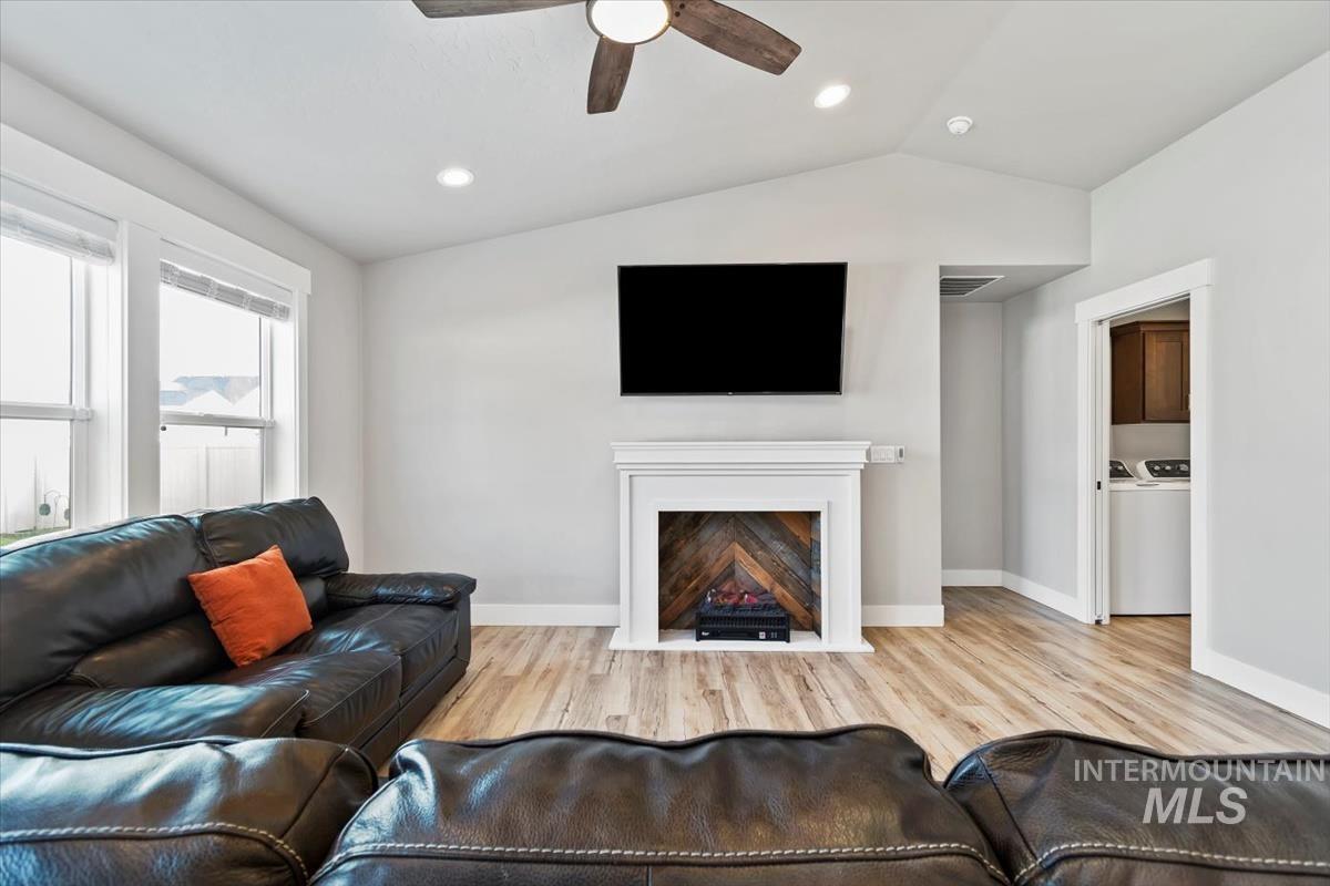 Living room featuring vaulted ceiling, light wood finished floors, ceiling fan, recessed lighting, and washing machine and clothes dryer