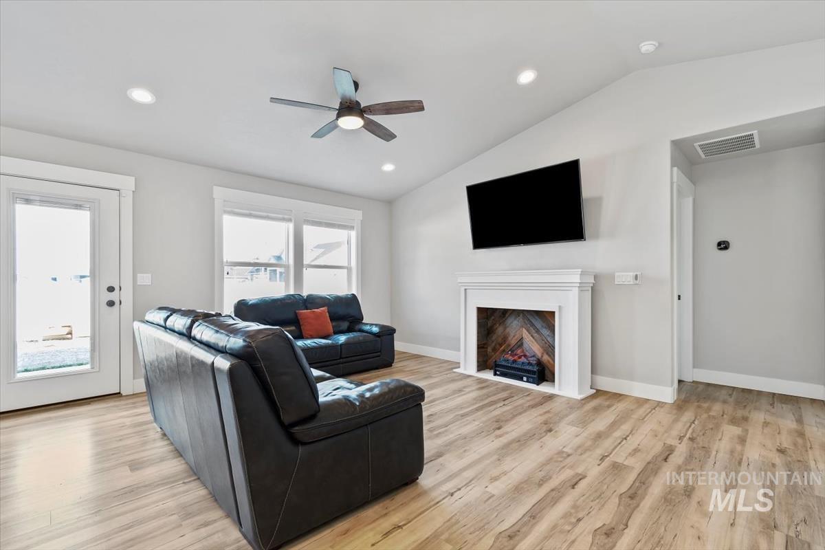 Living room with lofted ceiling, a ceiling fan, light wood-style flooring, a fireplace with flush hearth, and recessed lighting