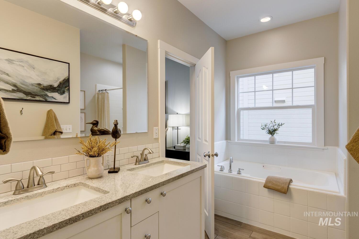 Full bathroom with double vanity, a bath, curtained shower, backsplash, and light wood finished floors