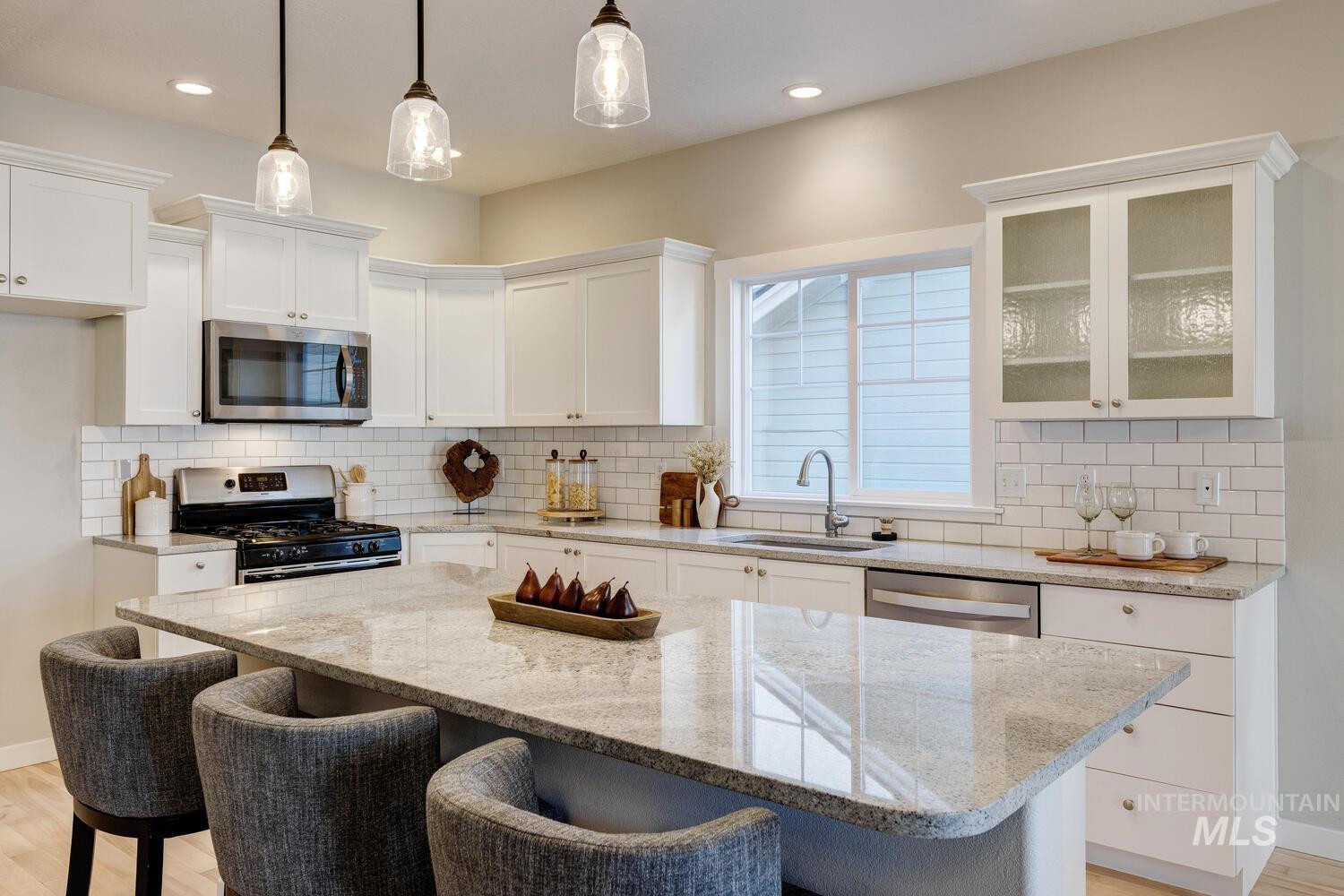 Kitchen with light wood-style floors, light stone countertops, appliances with stainless steel finishes, a breakfast bar, and white cabinets