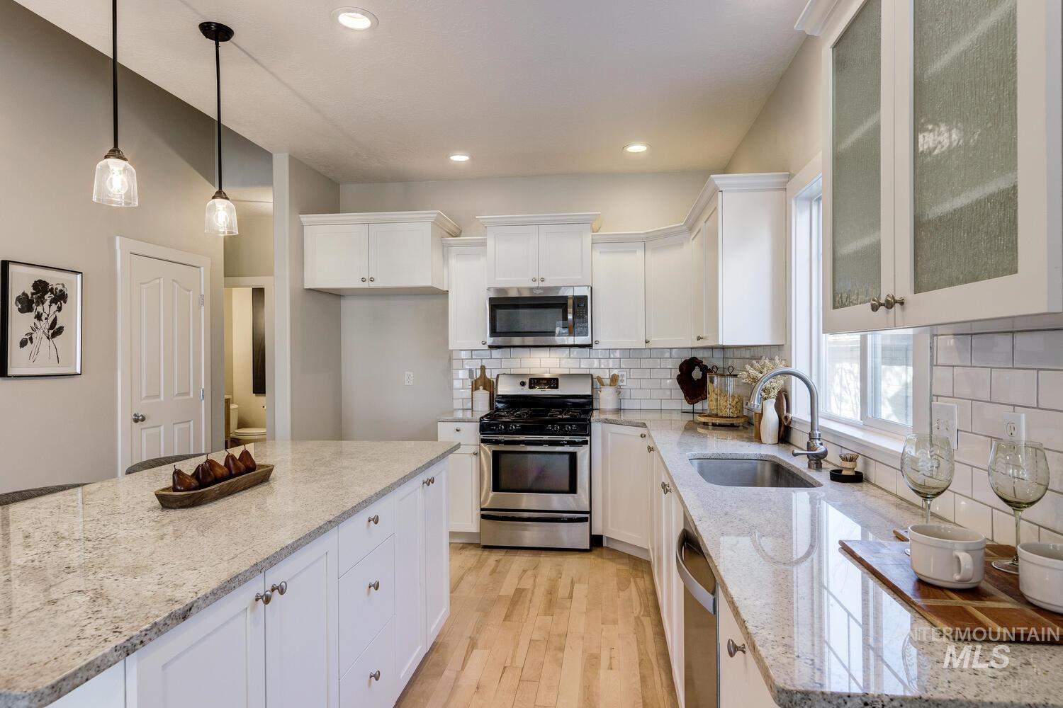 Kitchen featuring stainless steel appliances, white cabinetry, light stone counters, light wood-style floors, and recessed lighting