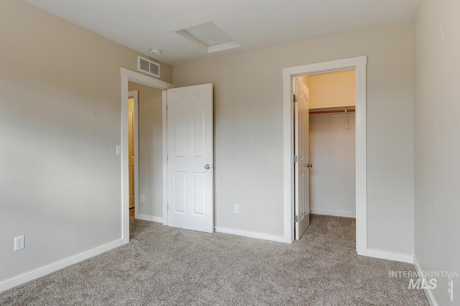 Unfurnished bedroom featuring a walk in closet, light colored carpet, and attic access