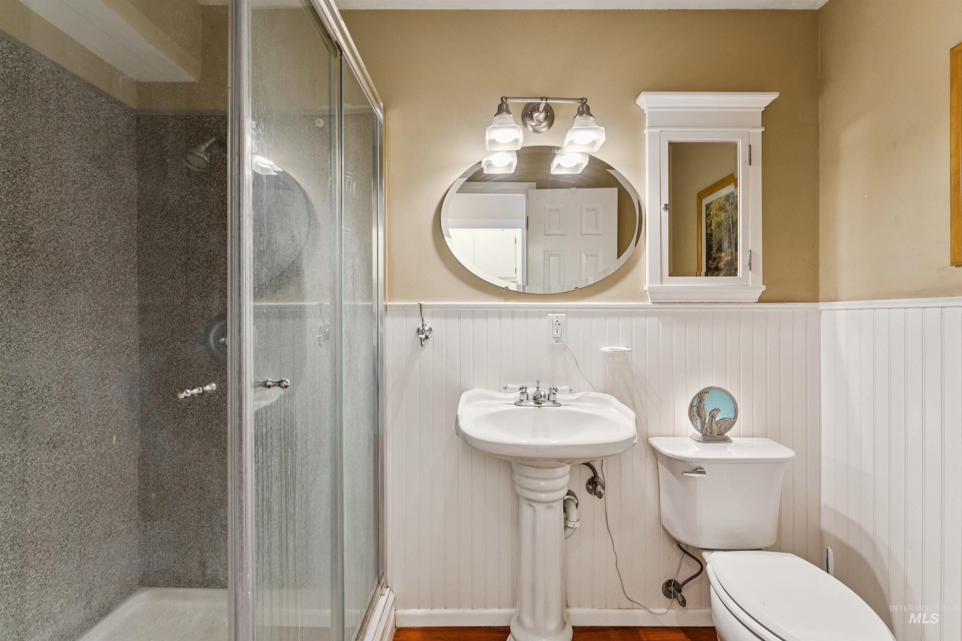Bathroom featuring a glass-enclosed shower with textured wall tile, a pedestal sink, and wainscoting