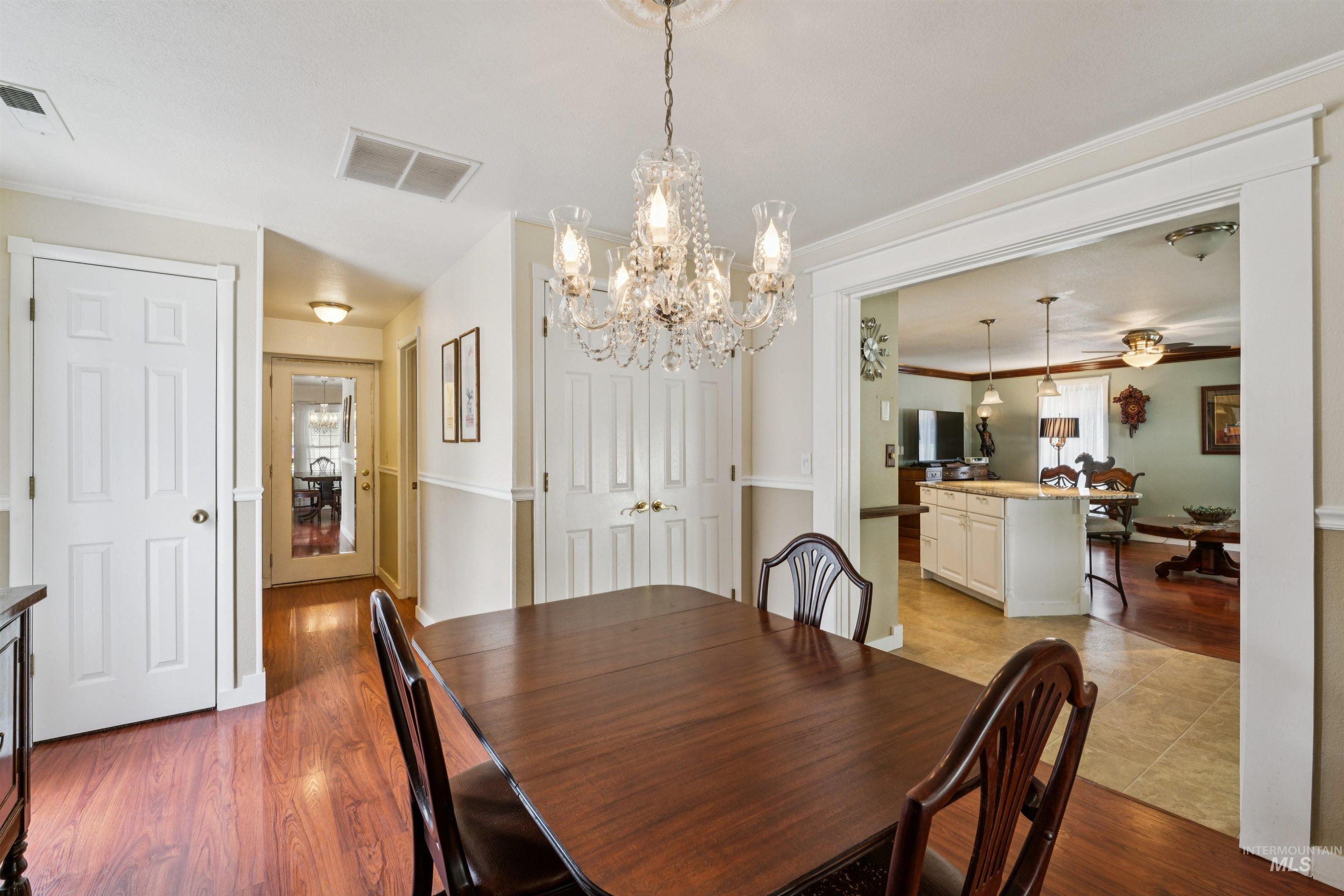 Dining area featuring a chandelier with crystal accents, wood-finish flooring, and an open doorway to another room