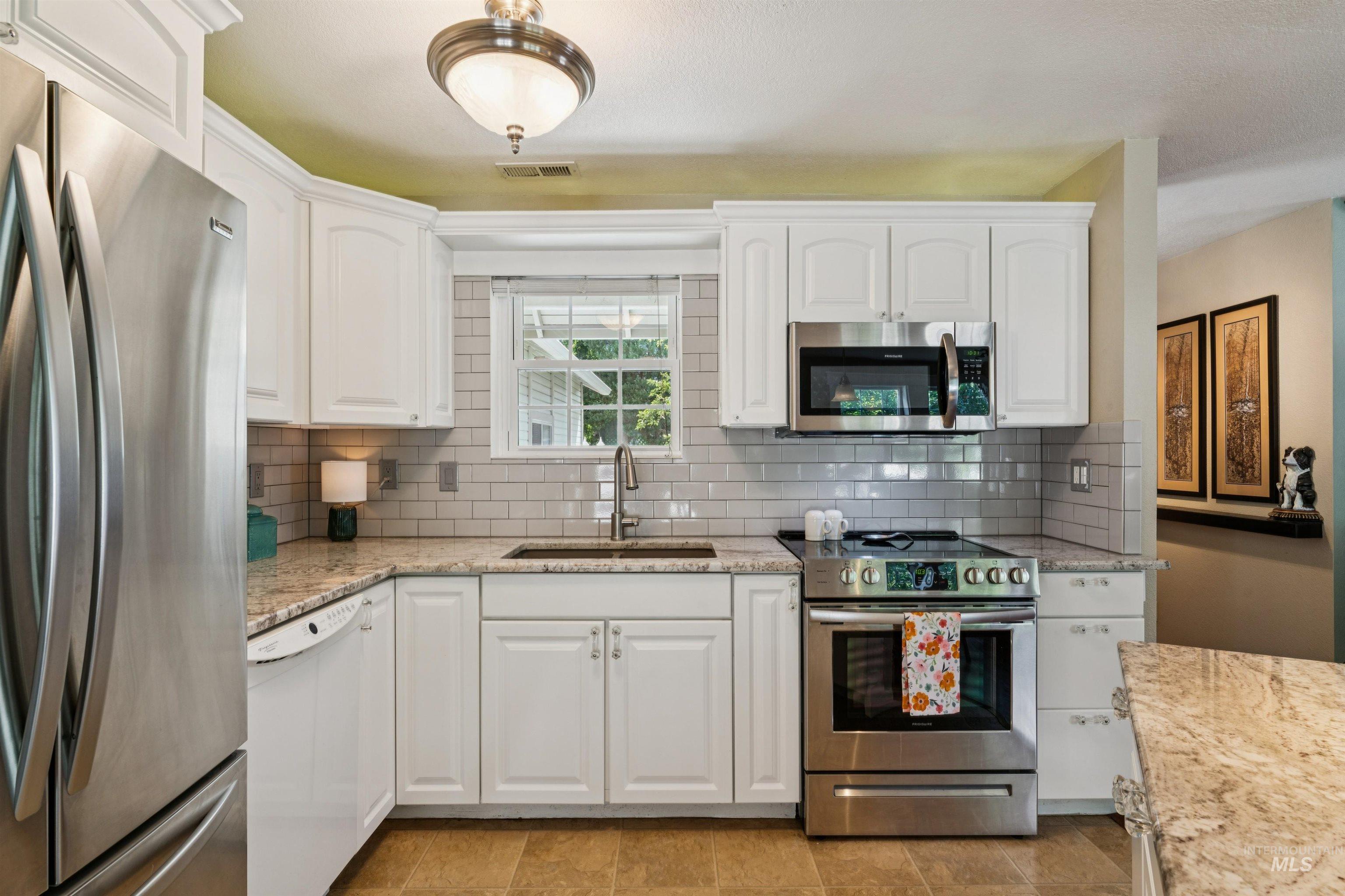 Kitchen featuring white cabinetry, stainless steel appliances, a white subway tile backsplash, and light-toned countertop surfaces