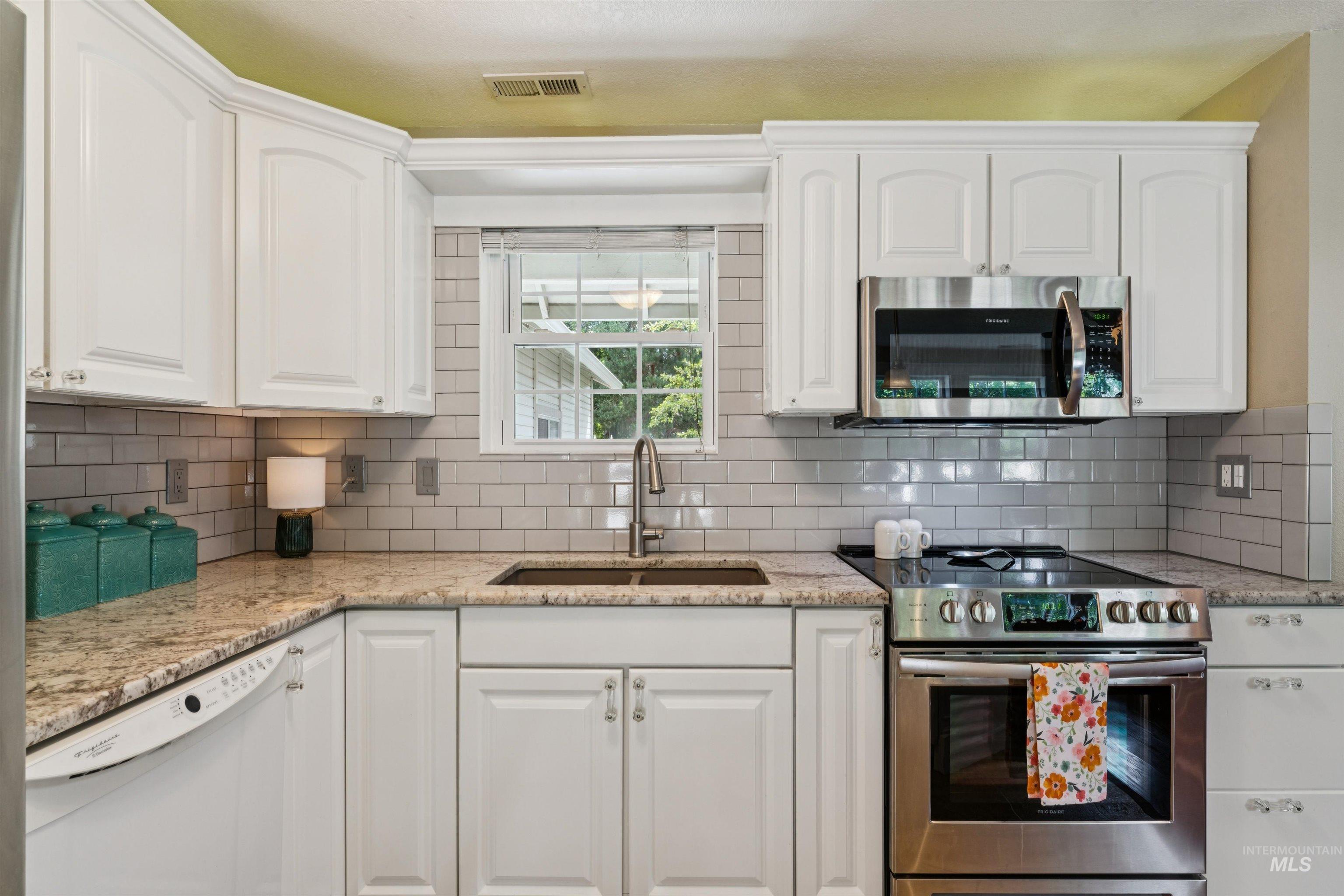 Kitchen featuring white cabinetry, light-toned countertops, subway tile backsplash, stainless steel appliances, and a double basin sink with a gooseneck faucet