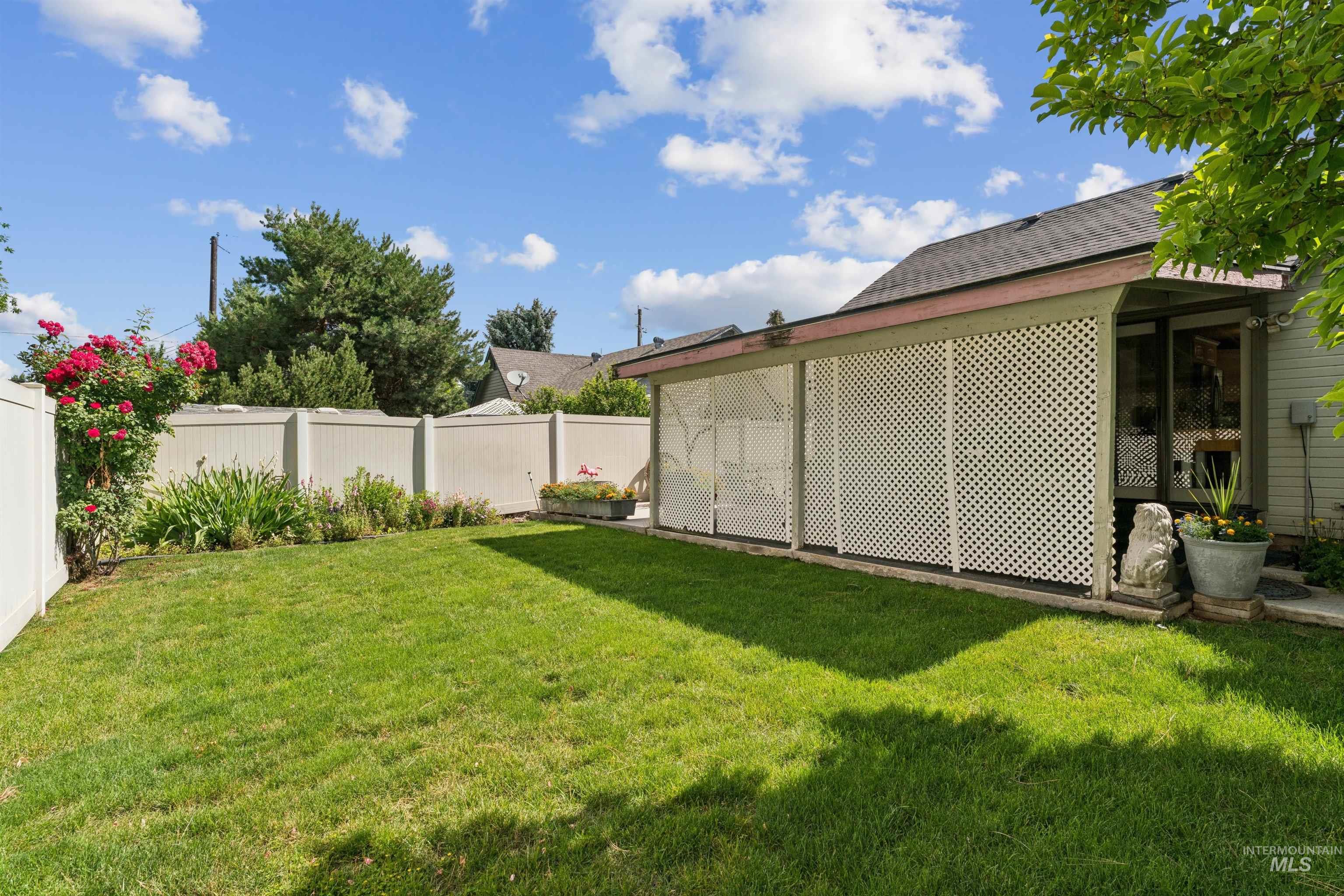 Rear exterior featuring a covered patio with lattice panels, a vibrant green lawn, and a light-colored privacy fence
