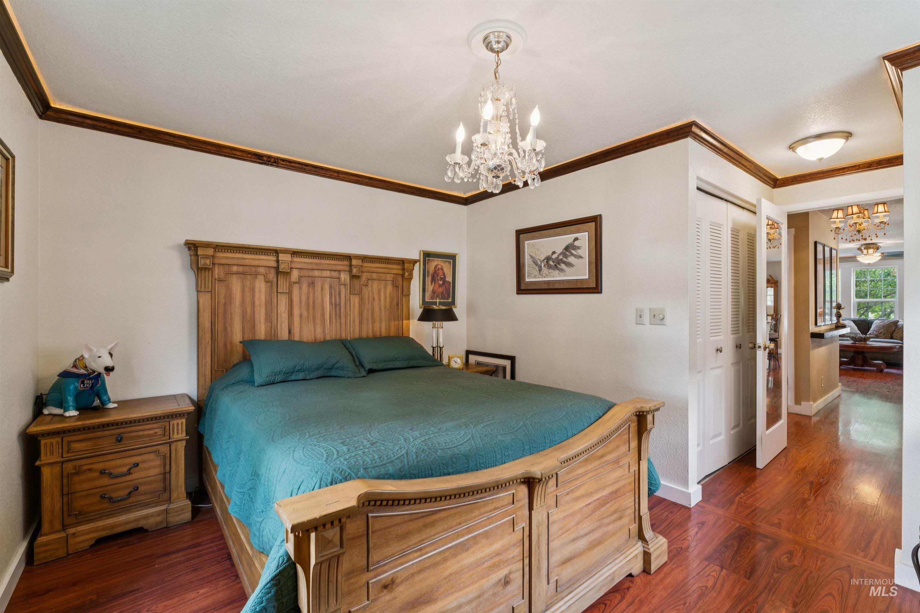 Spacious room featuring wood-finish flooring, a crystal chandelier, and crown molding