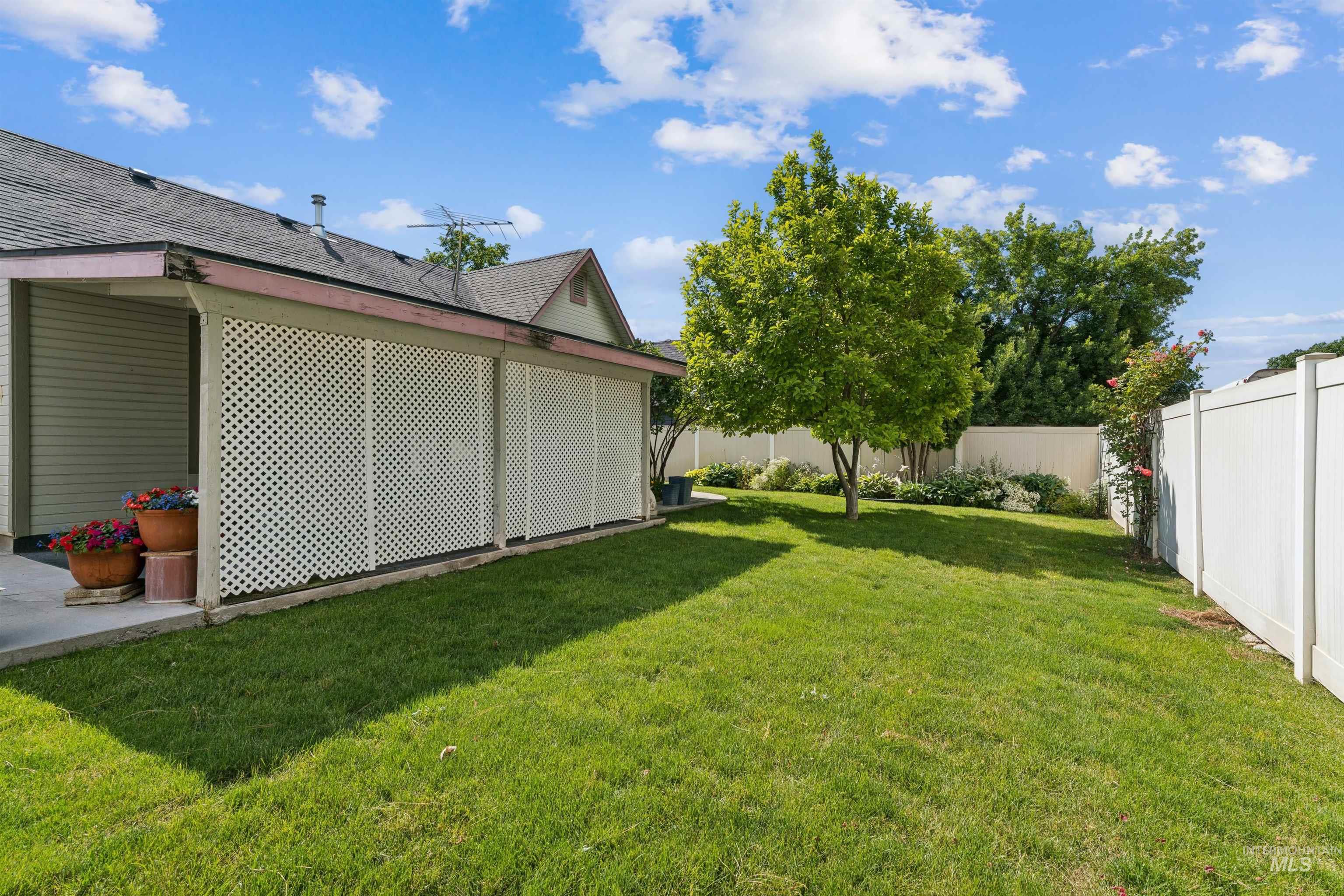 Expansive backyard featuring a manicured lawn, a mature tree, and a white vinyl privacy fence