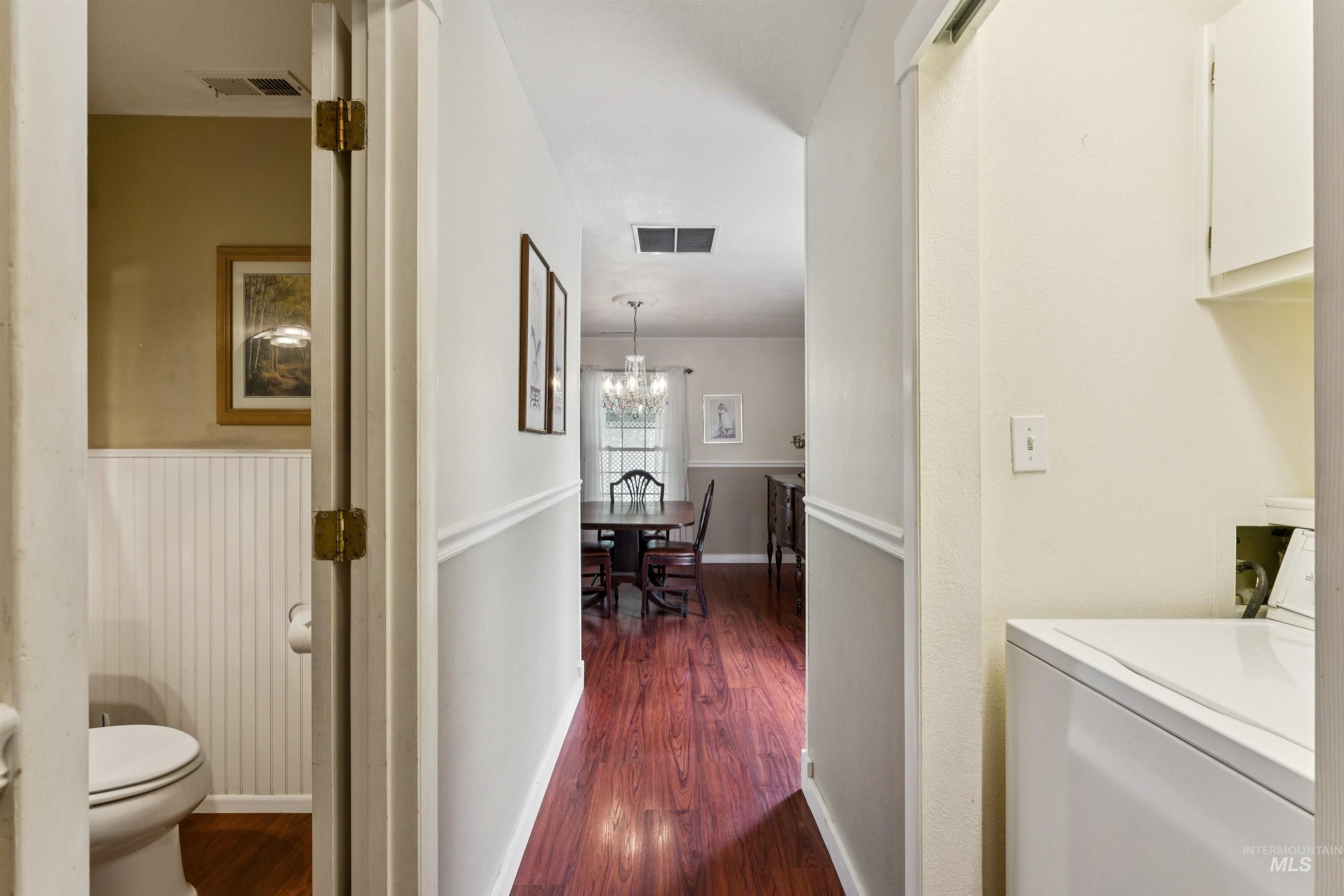 Hallway featuring wood-finish flooring, white wainscoting, and crown molding