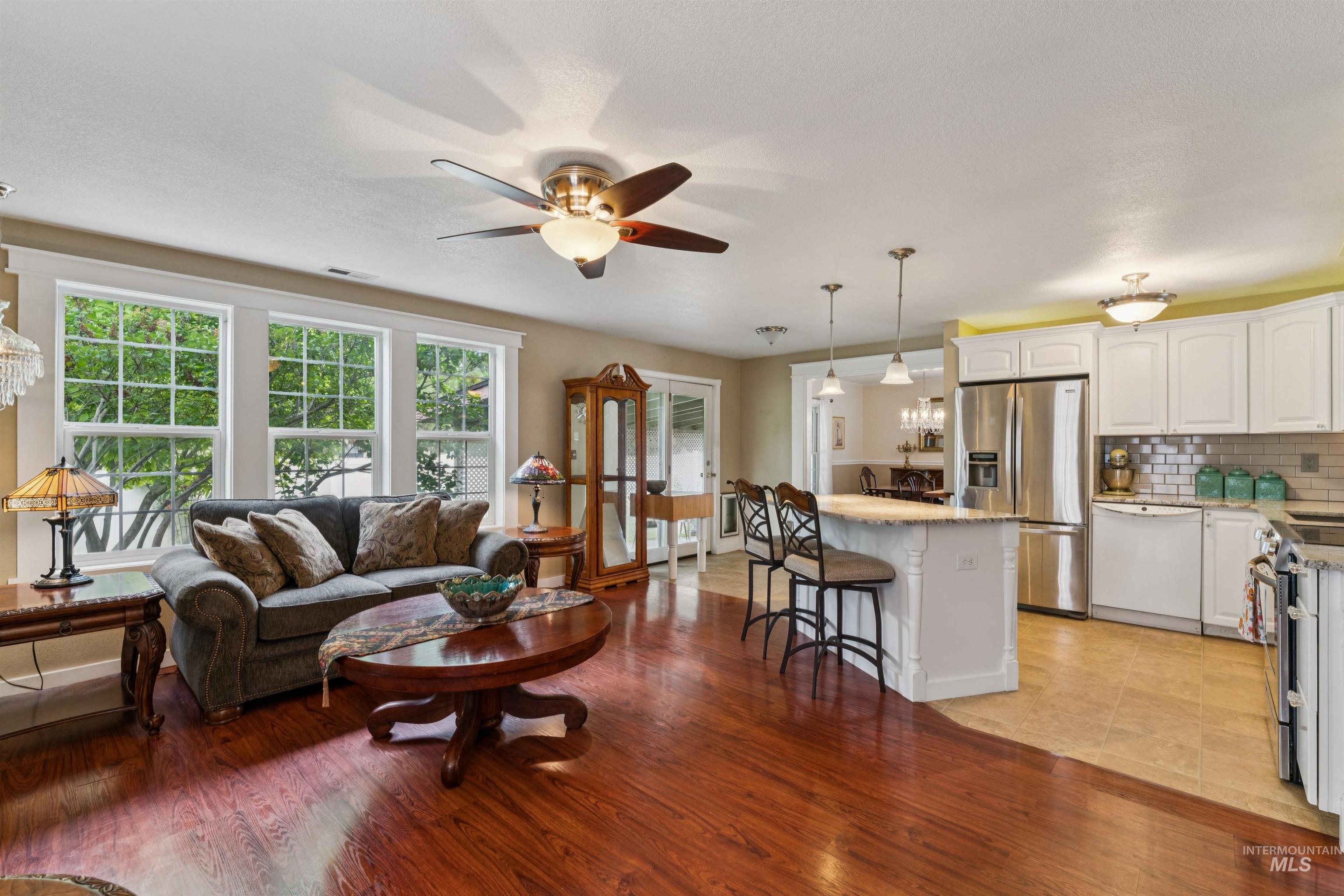 Open-concept living area featuring rich wood-finish flooring, a ceiling fan with integrated lighting, and multiple windows