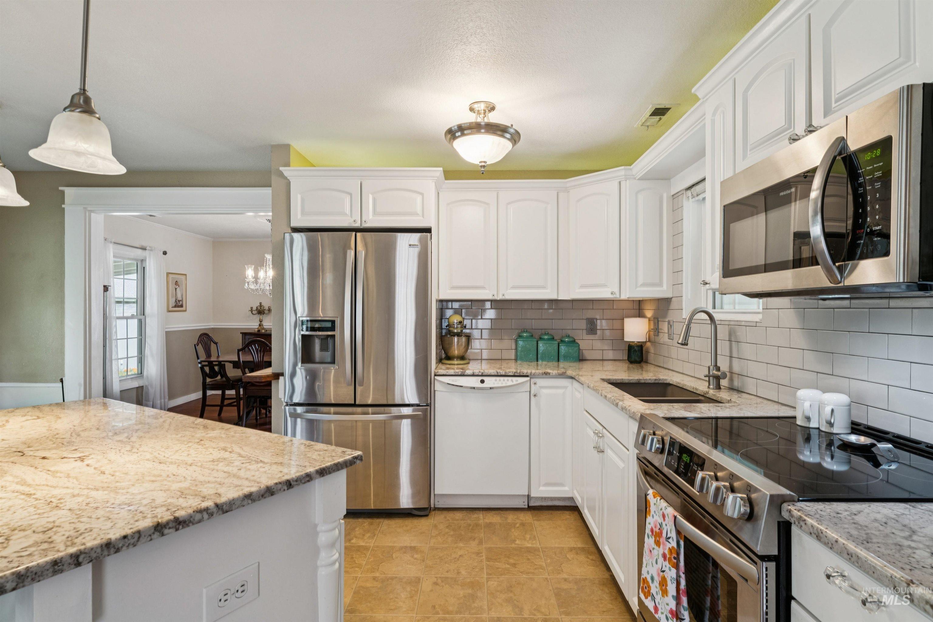 Kitchen featuring white cabinetry, stainless steel appliances, granite countertops, and subway tile backsplash