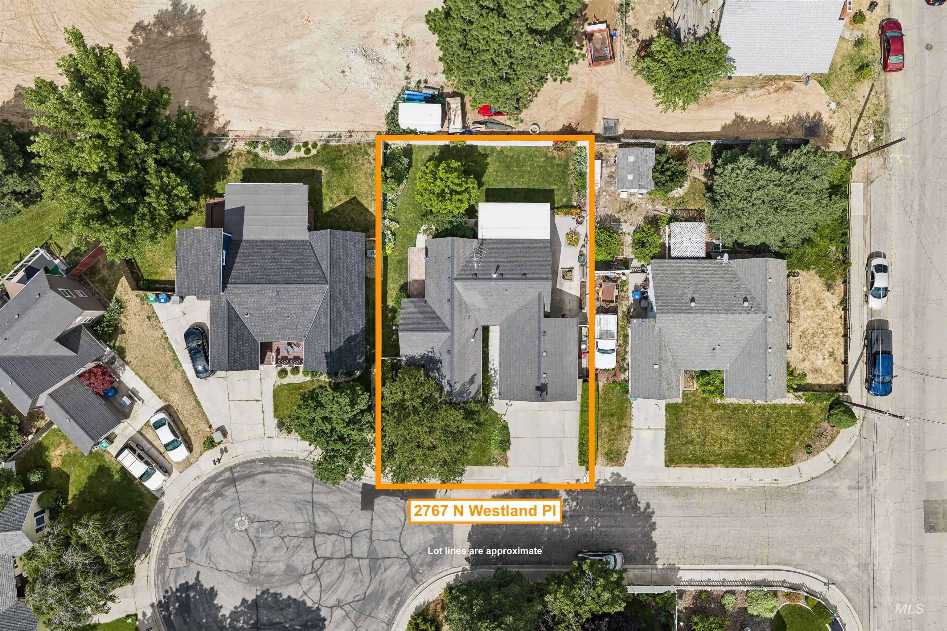 Aerial view of a residential property featuring a gray shingle roof, a paved driveway, and a partially grassed yard