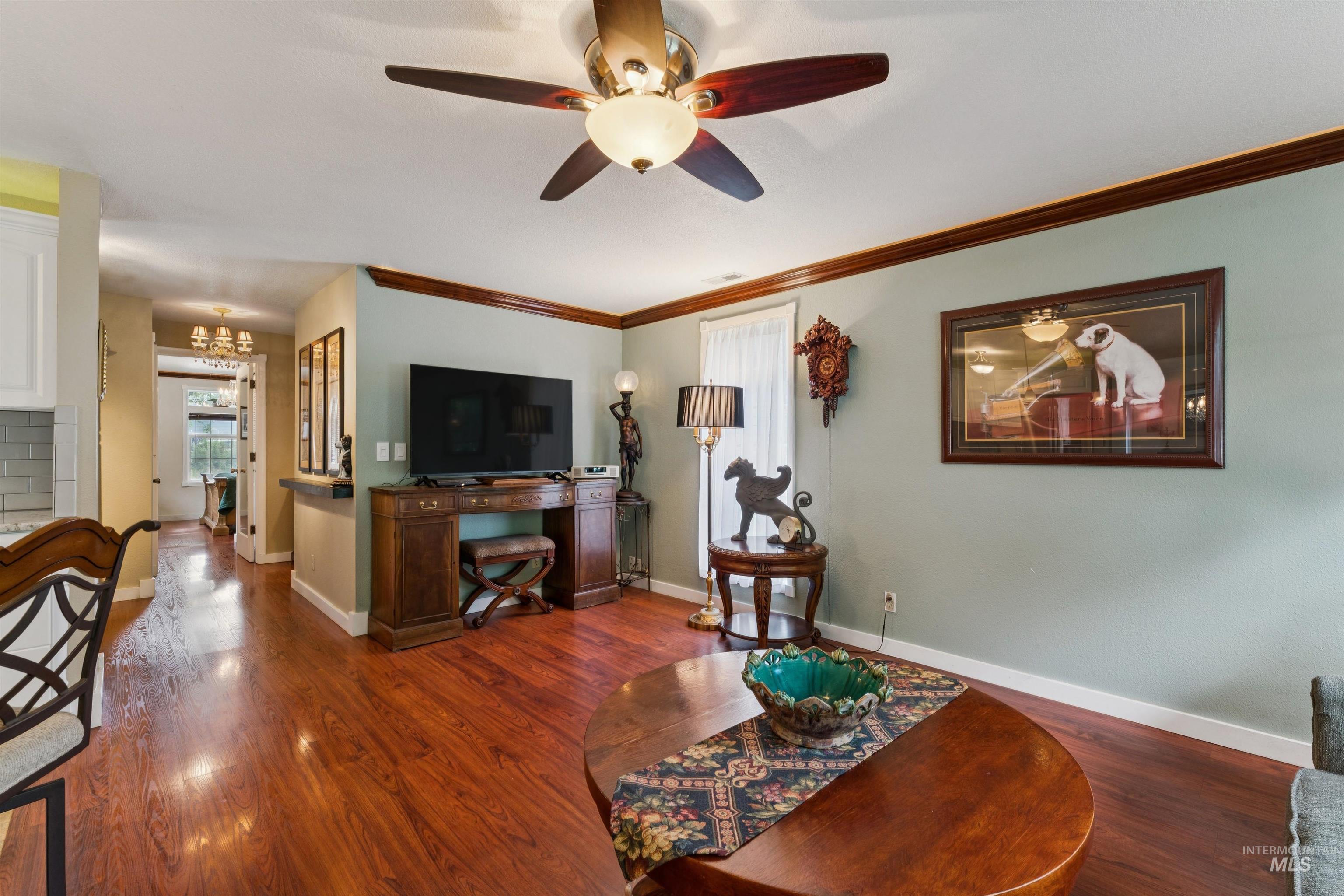 Living area featuring wood-finish flooring, a ceiling fan with integrated lighting, and crown molding