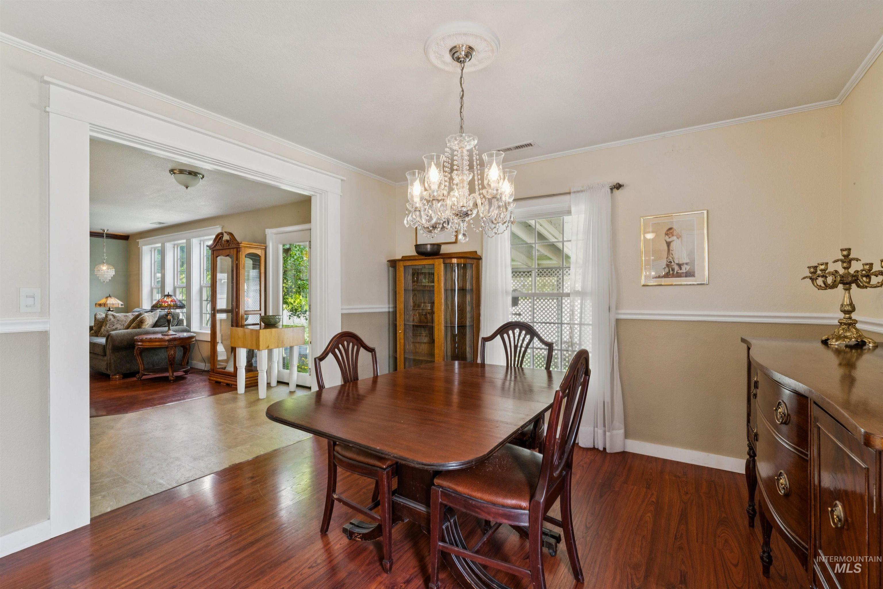Dining area featuring wood-finish flooring, a crystal chandelier with ceiling medallion, and white chair rail molding