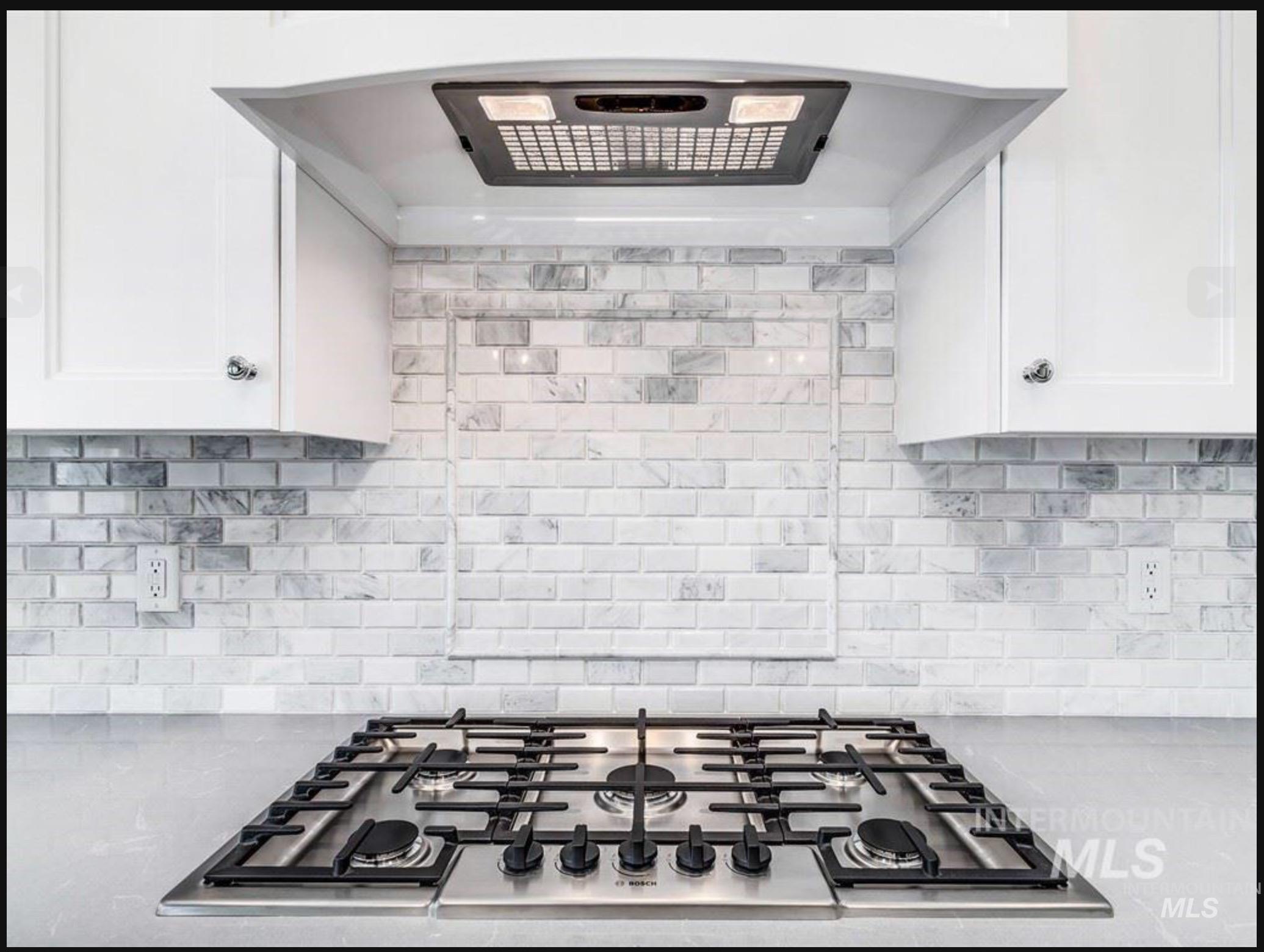 Kitchen featuring ventilation hood, stainless steel gas cooktop, light stone countertops, and white cabinetry