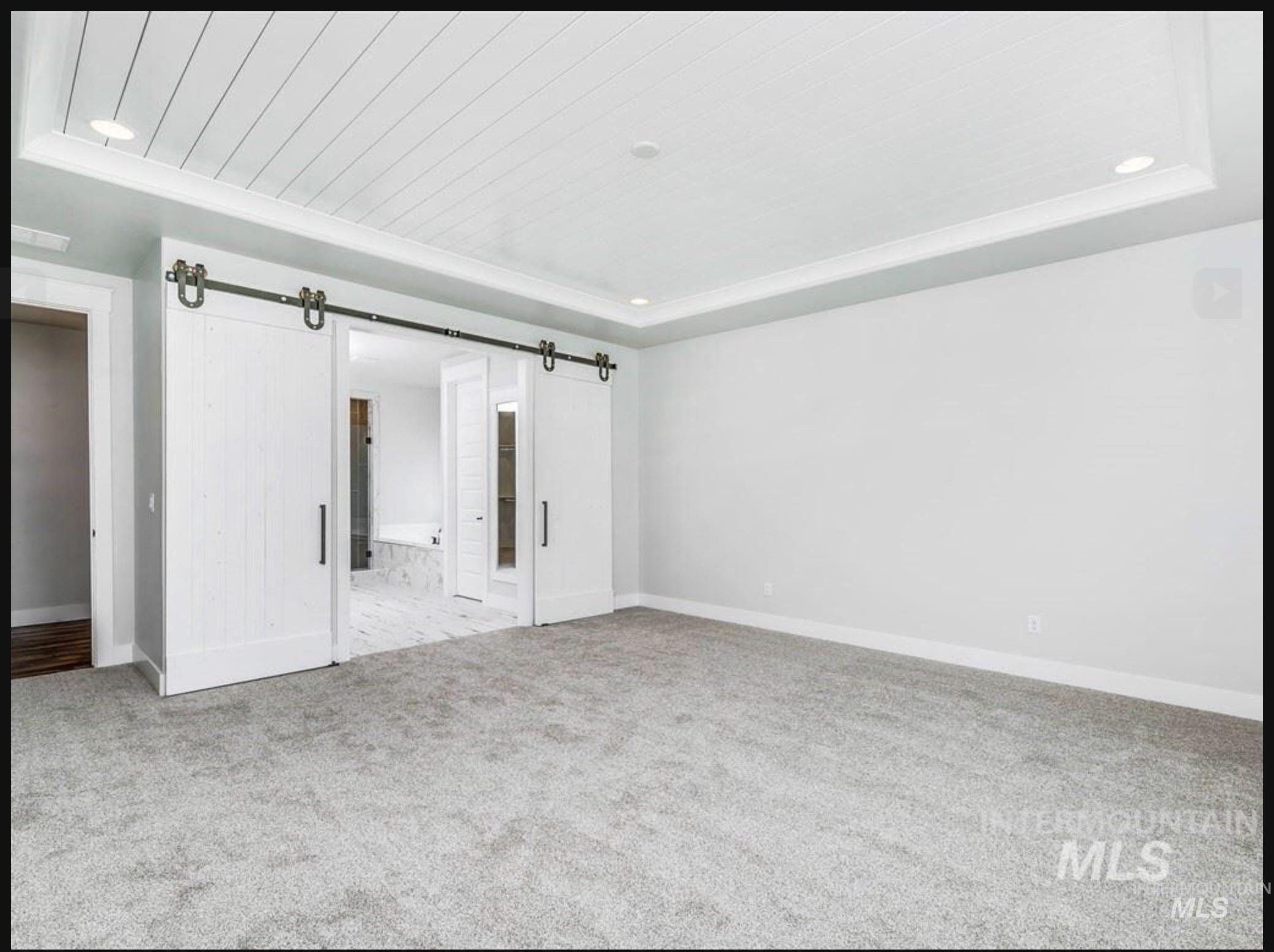 Unfurnished bedroom with a barn door, ensuite bathroom, light carpet, recessed lighting, and a tray ceiling