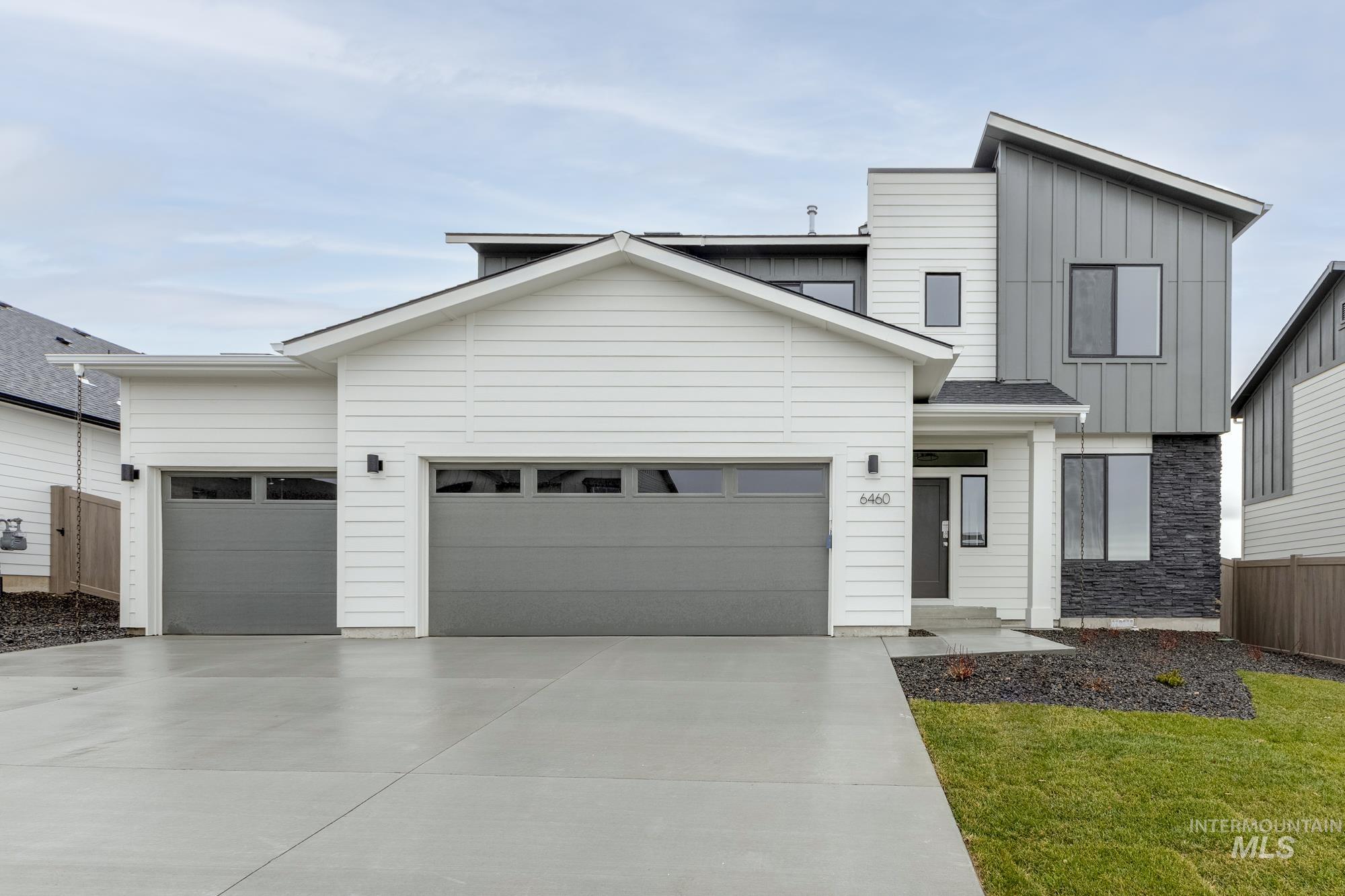 View of front of home with board and batten siding, concrete driveway, an attached garage, and stone siding