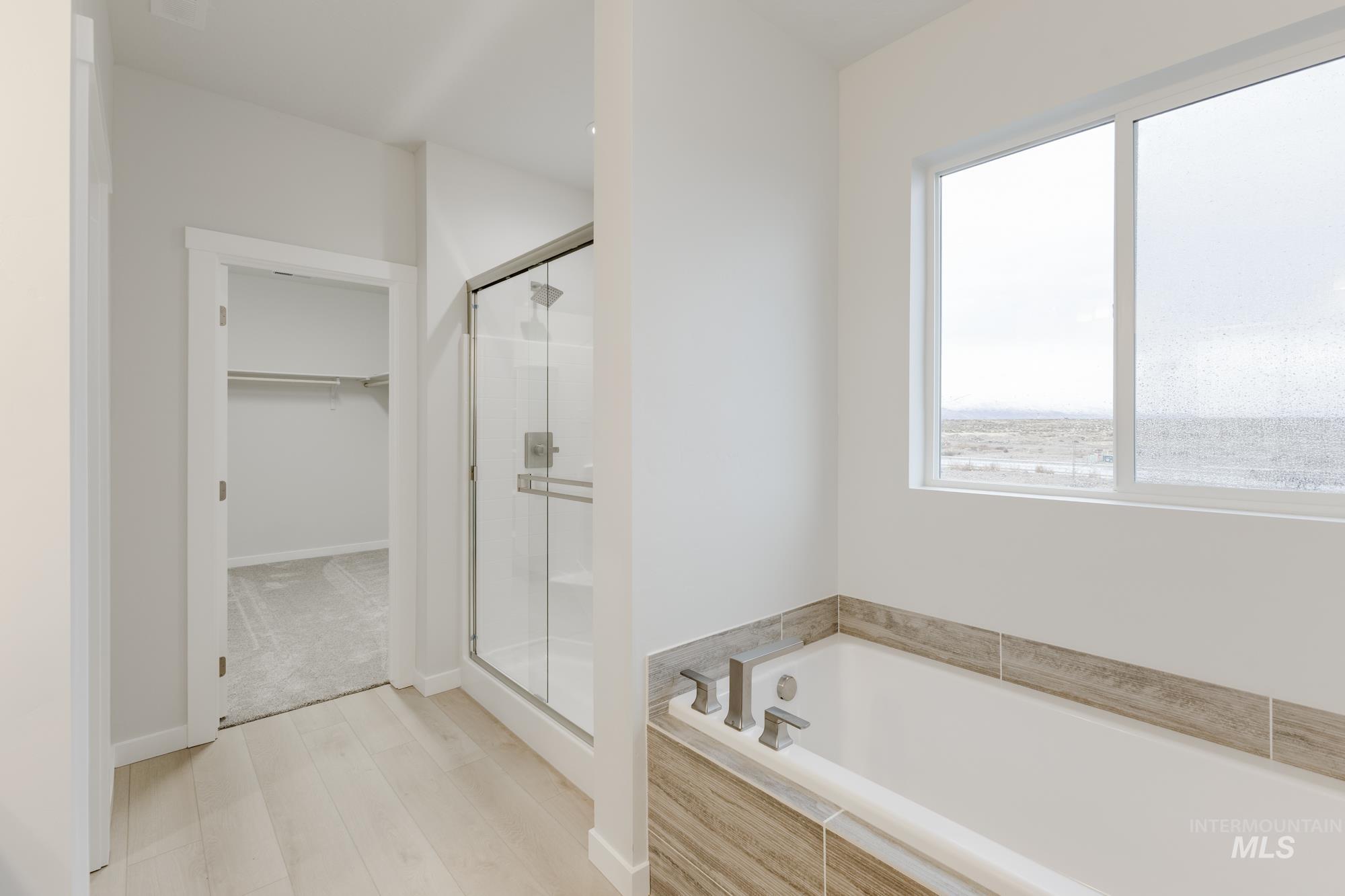 Bathroom featuring a bath, a spacious closet, a stall shower, and light wood finished floors