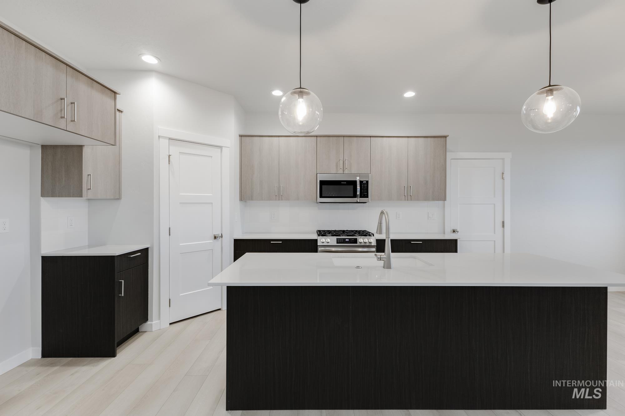 Kitchen featuring hanging light fixtures, modern cabinets, stainless steel appliances, light stone counters, and an island with sink
